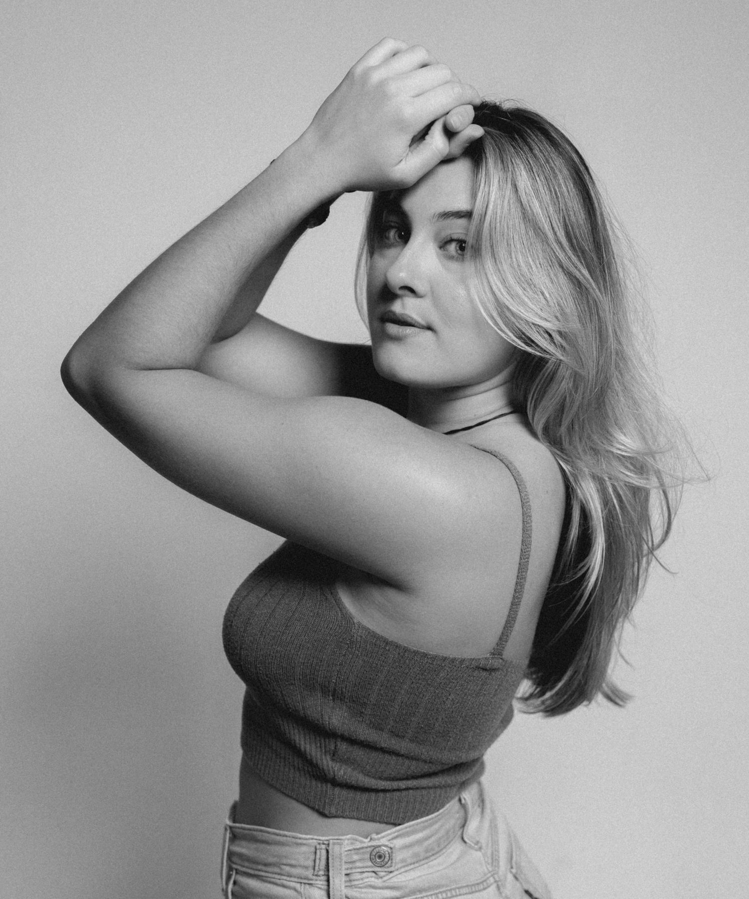Black and white photo of blonde woman in ribbed crop top posing with hand raised to forehead.