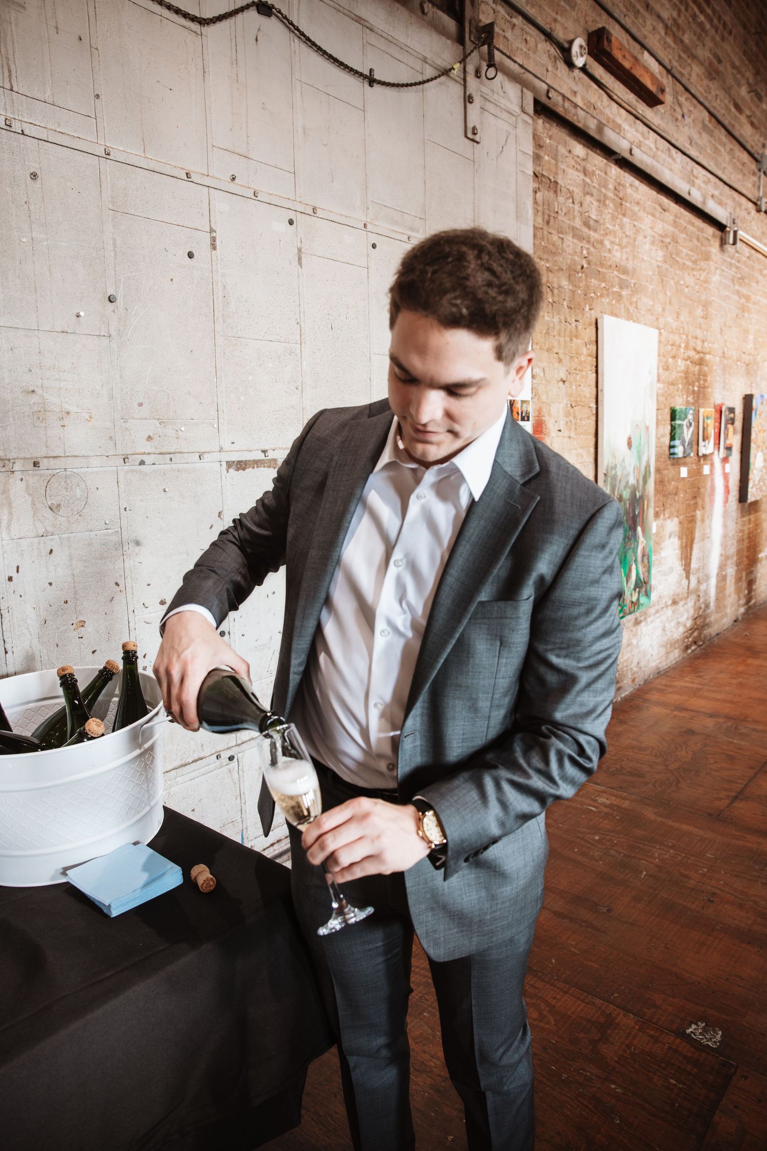 Young man in gray suit carefully pours champagne into a glass at an elegant event.
