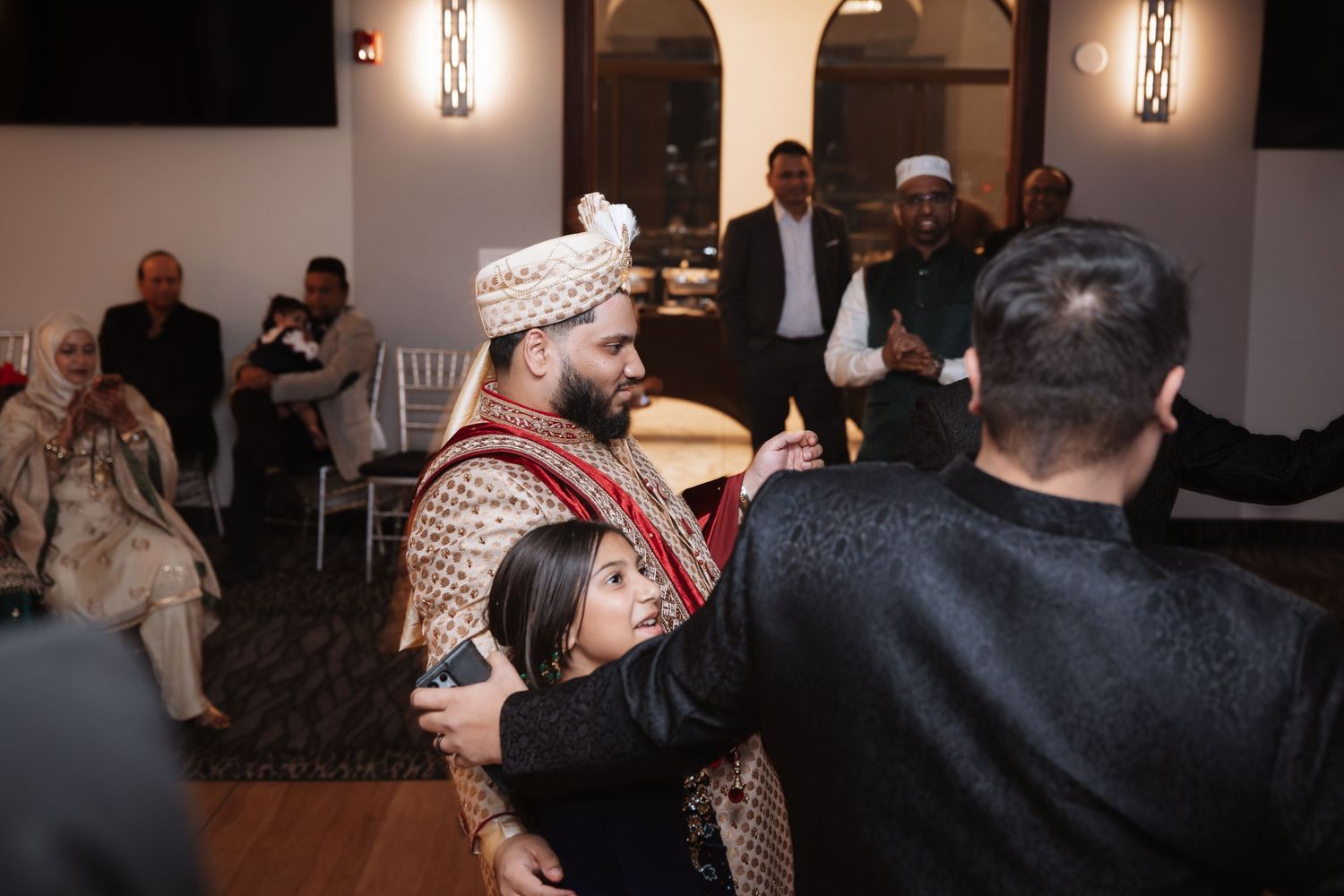 Man in traditional South Asian attire embracing a child at a wedding celebration.
