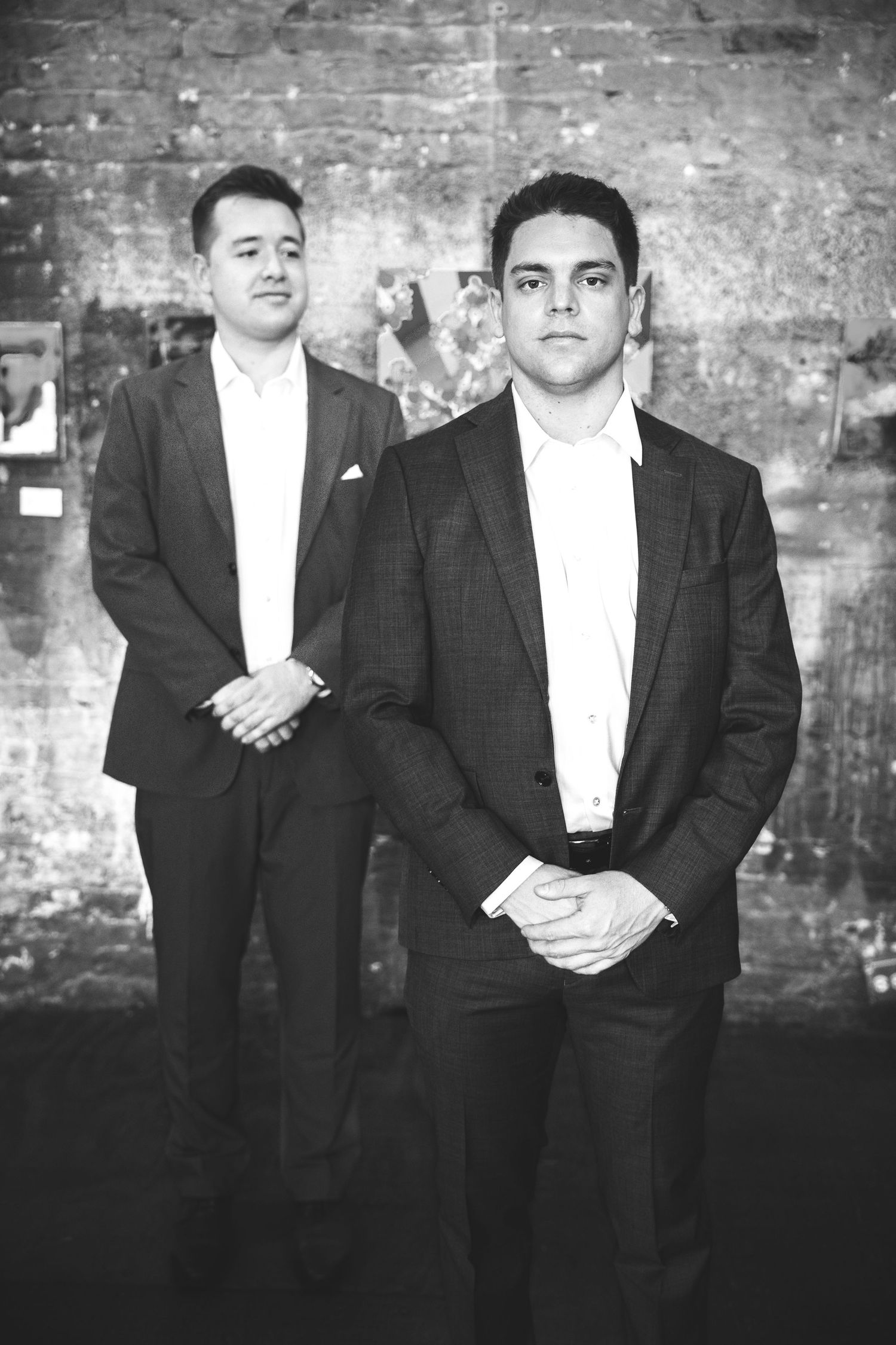 Black and white photo of two suited men posing seriously in an art gallery setting.