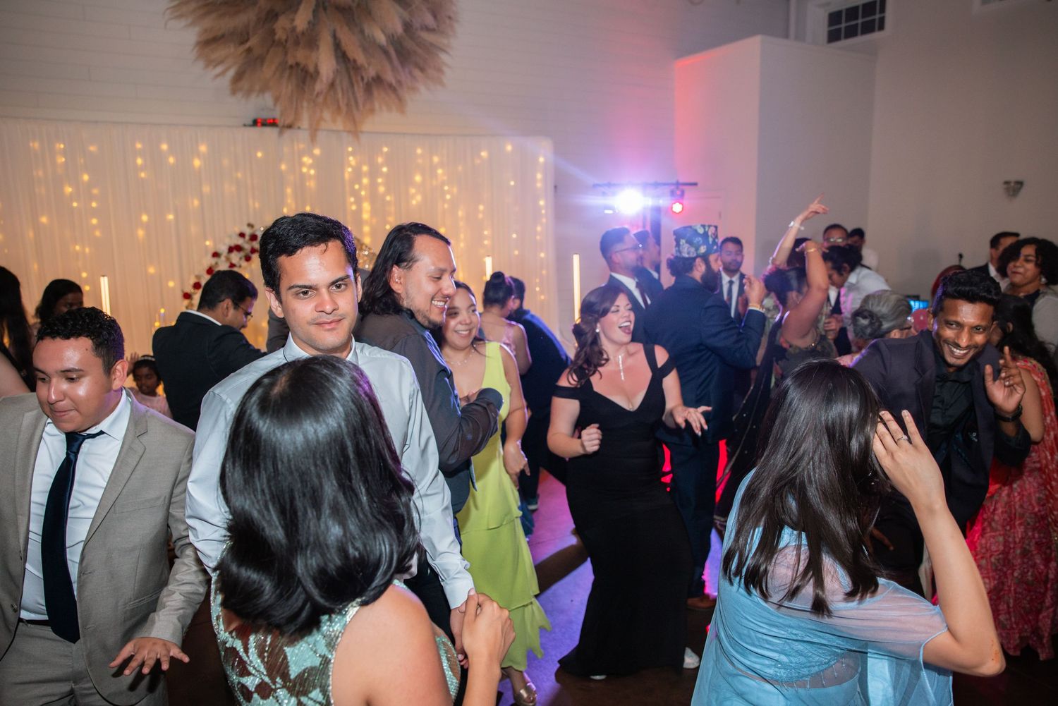 Elegantly dressed wedding guests dancing joyfully on the reception dance floor.
