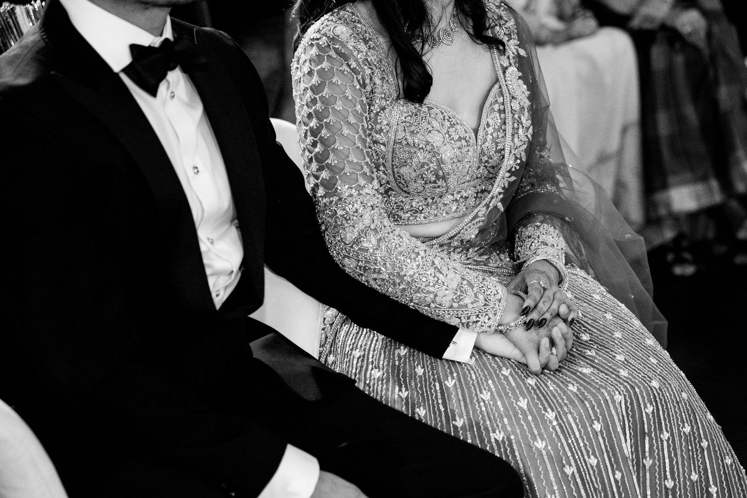 Couple holding hands in elegant wedding attire, black and white photo.