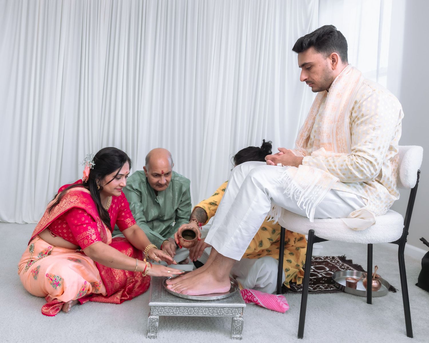Elderly couple washing grooms feet in silver tray during traditional Hindu wedding ritual ceremony.