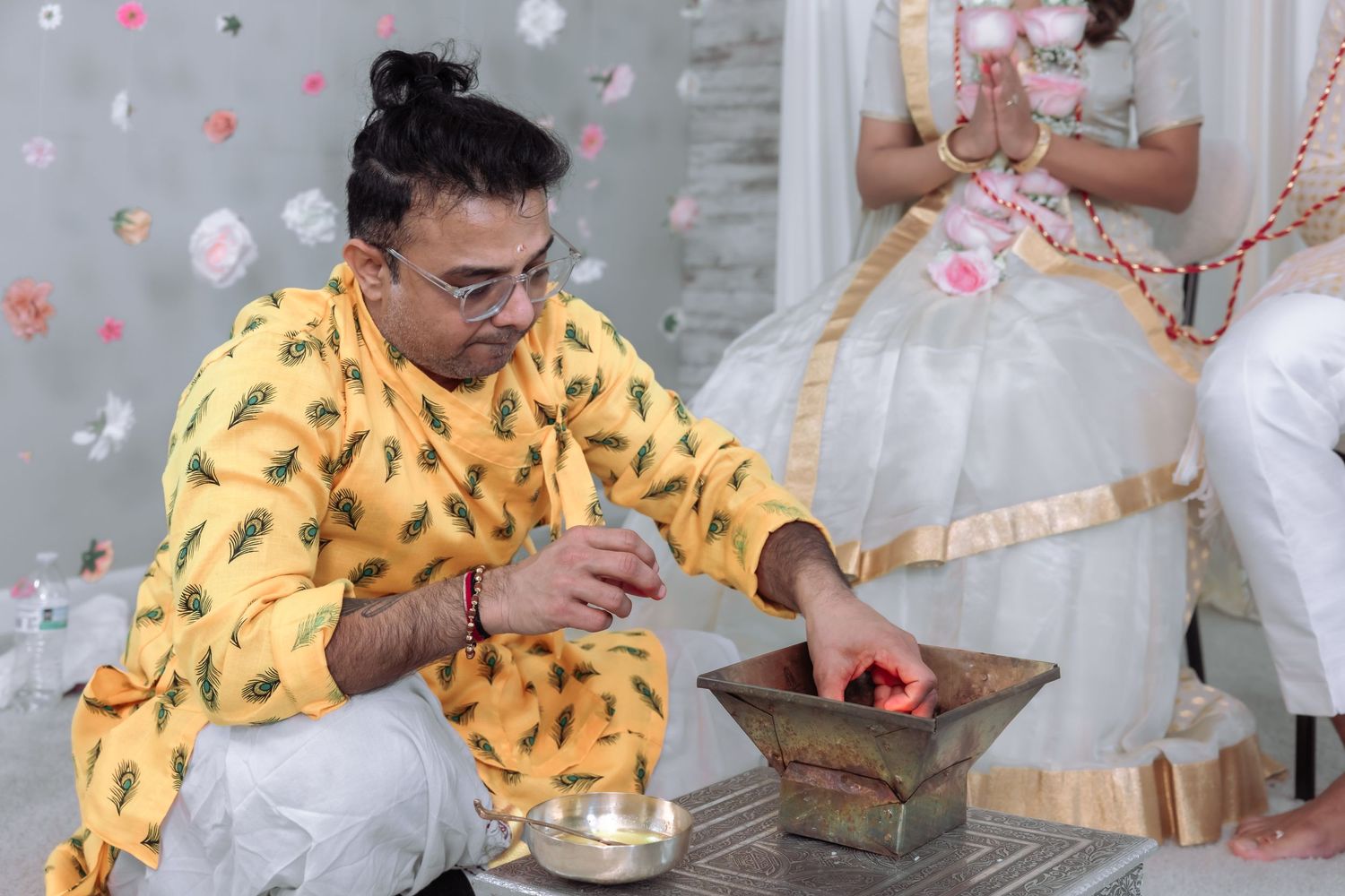 Hindu priest in yellow kurta performs sacred fire ritual during traditional Indian wedding ceremony.