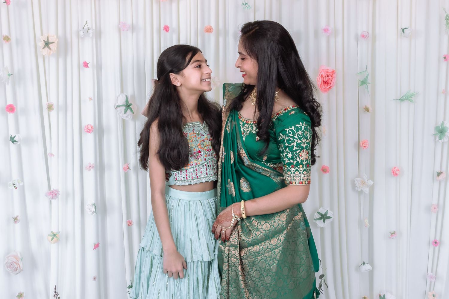 Mother and daughter in matching green Indian outfits share a joyful moment at festive celebration.