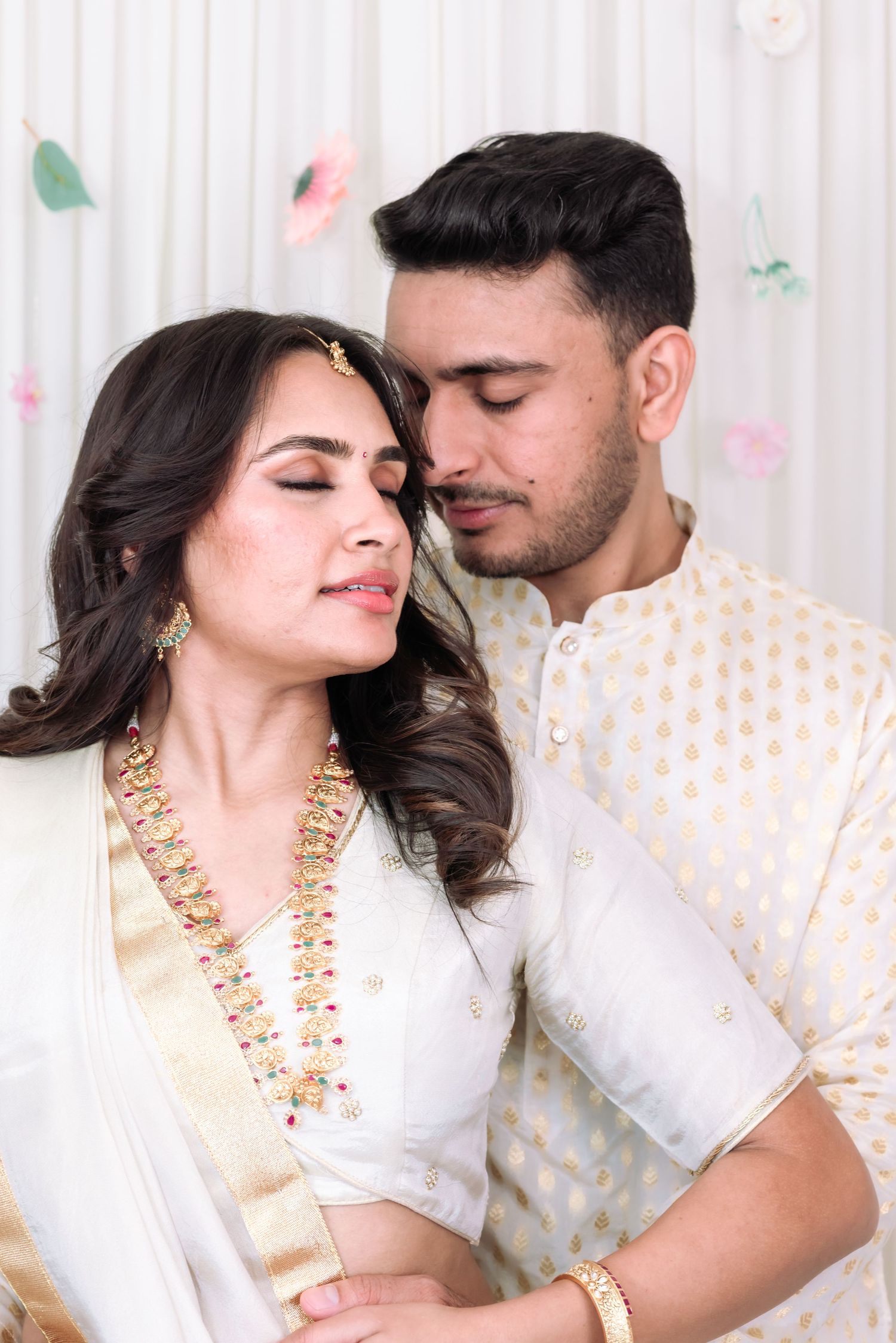 Indian couple in white and gold traditional outfits sharing an intimate moment at their engagement ceremony.