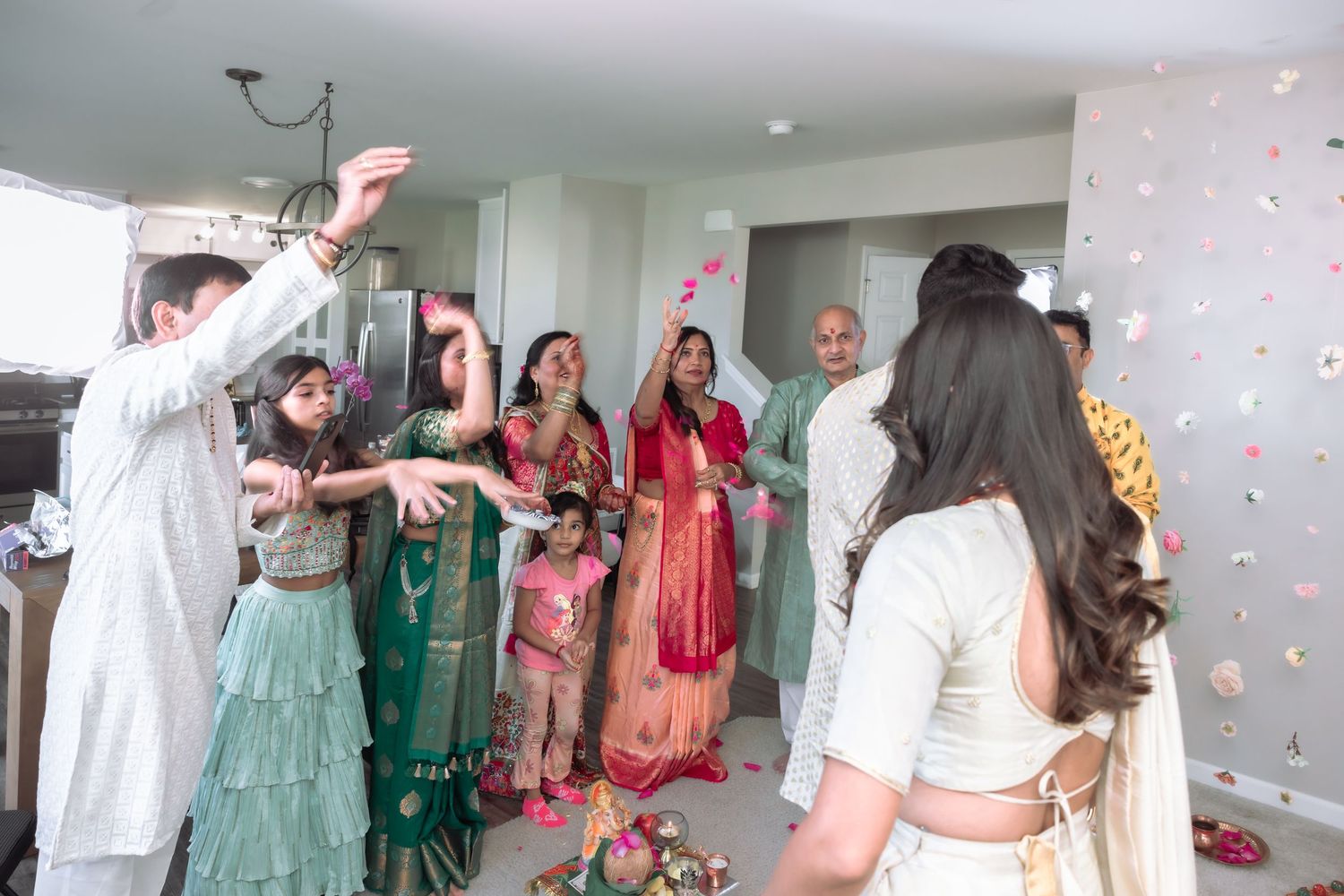 Joyful Indian wedding guests tossing flower petals in celebration indoors.