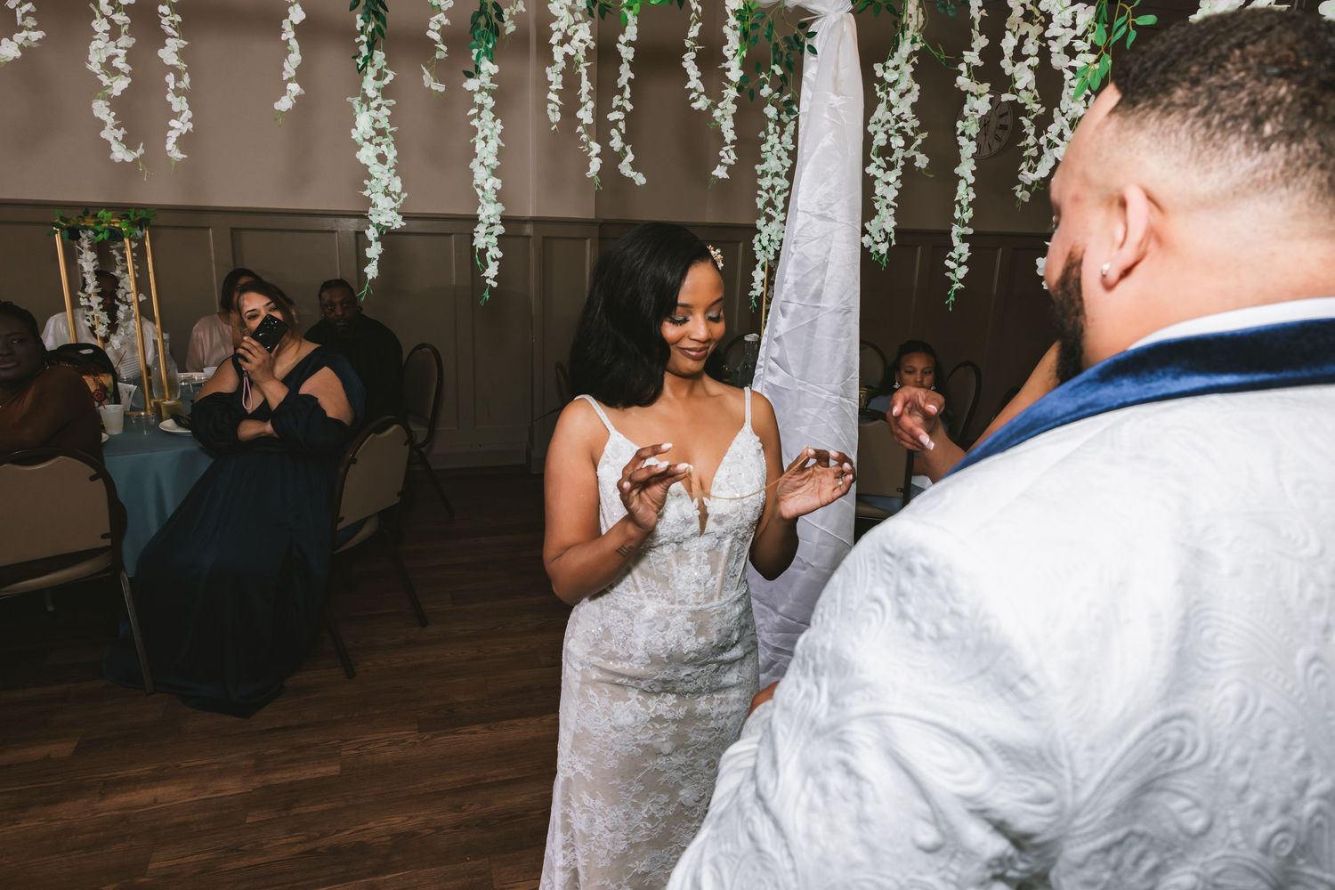 Bride in lace wedding gown smiling joyfully at groom during first dance at elegant wedding reception.