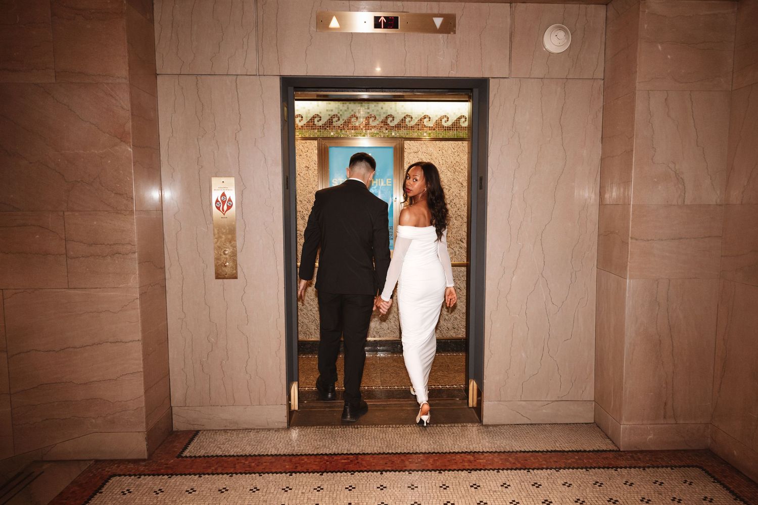 Couple in formal attire holding hands stepping into an elegant elevator with ornate gold interior.Chicago Wedding Photographer