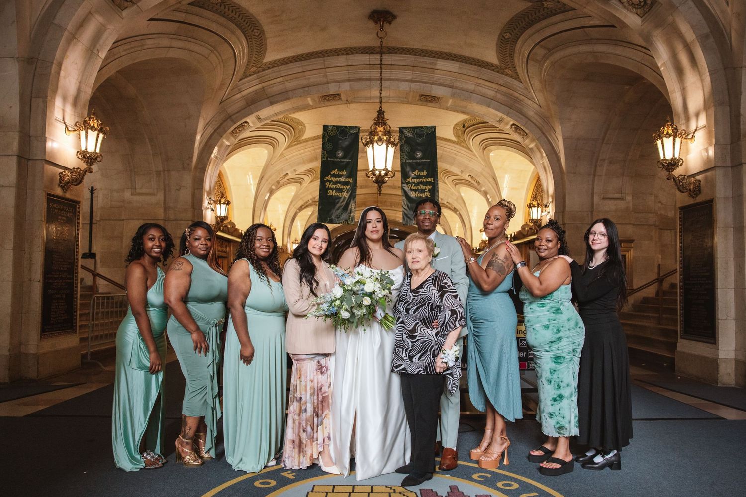 Bride poses with bridesmaids in teal dresses inside an elegant venue with ornate architecture and warm lighting.