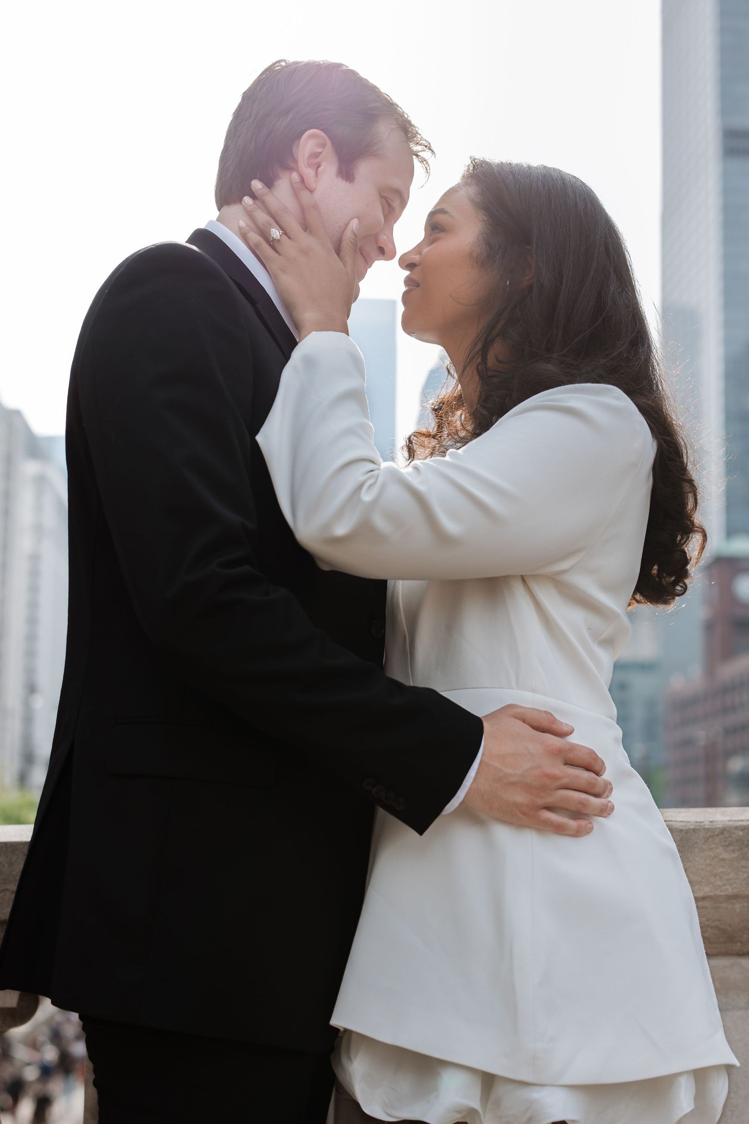 Romantic couple nearly kissing while embracing on an outdoor terrace with a glowing city skyline backdrop.