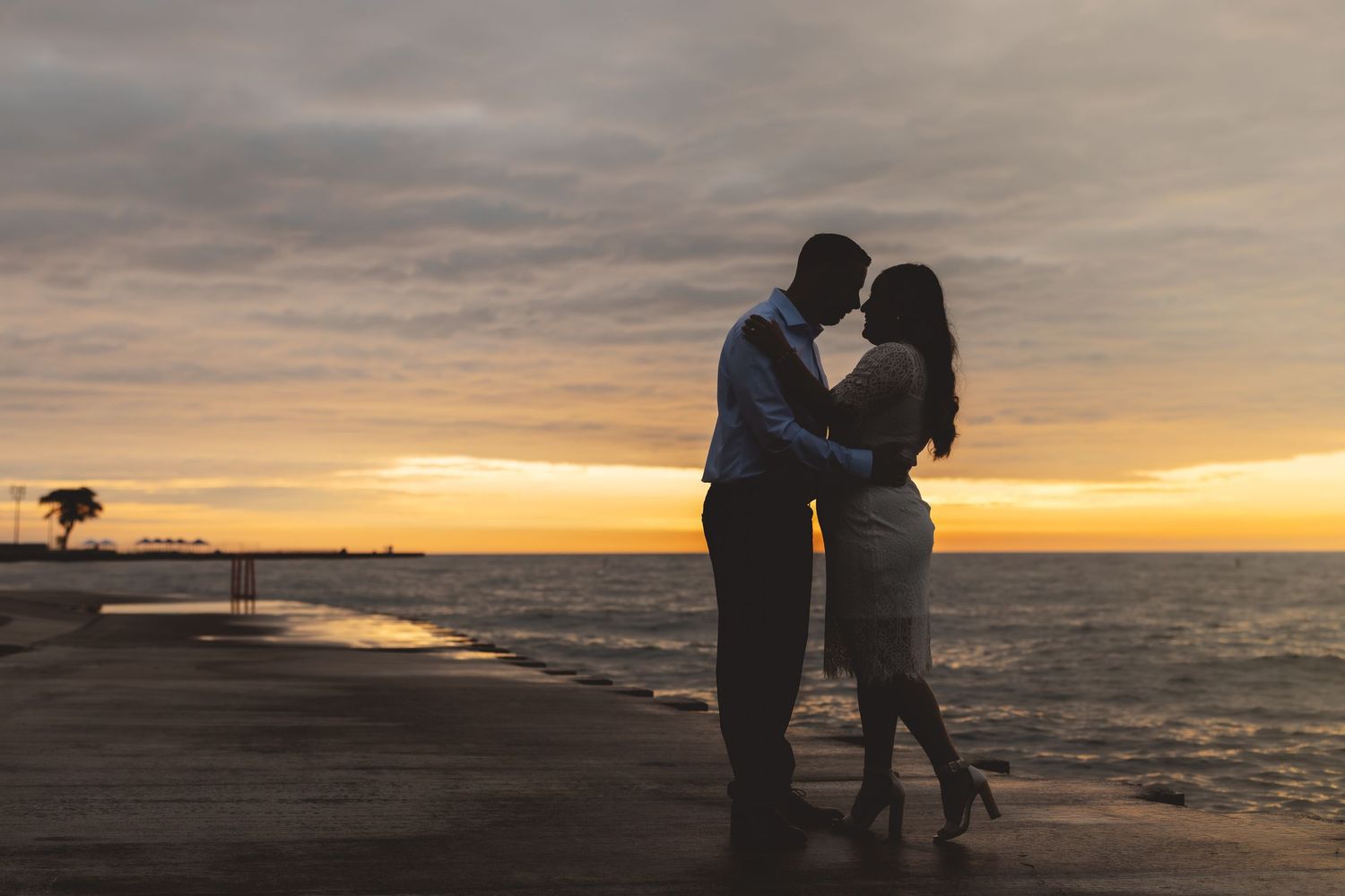 Romantic couple silhouette kissing at sunset on a lakeside pier with colorful sky.