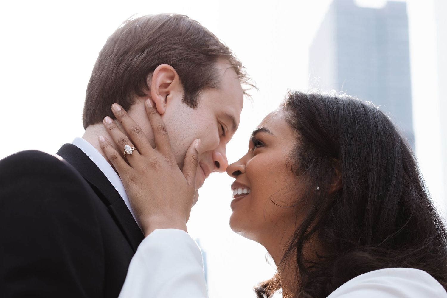 Happy interracial couple sharing an intimate moment, smiling and touching foreheads against a city skyline backdrop.