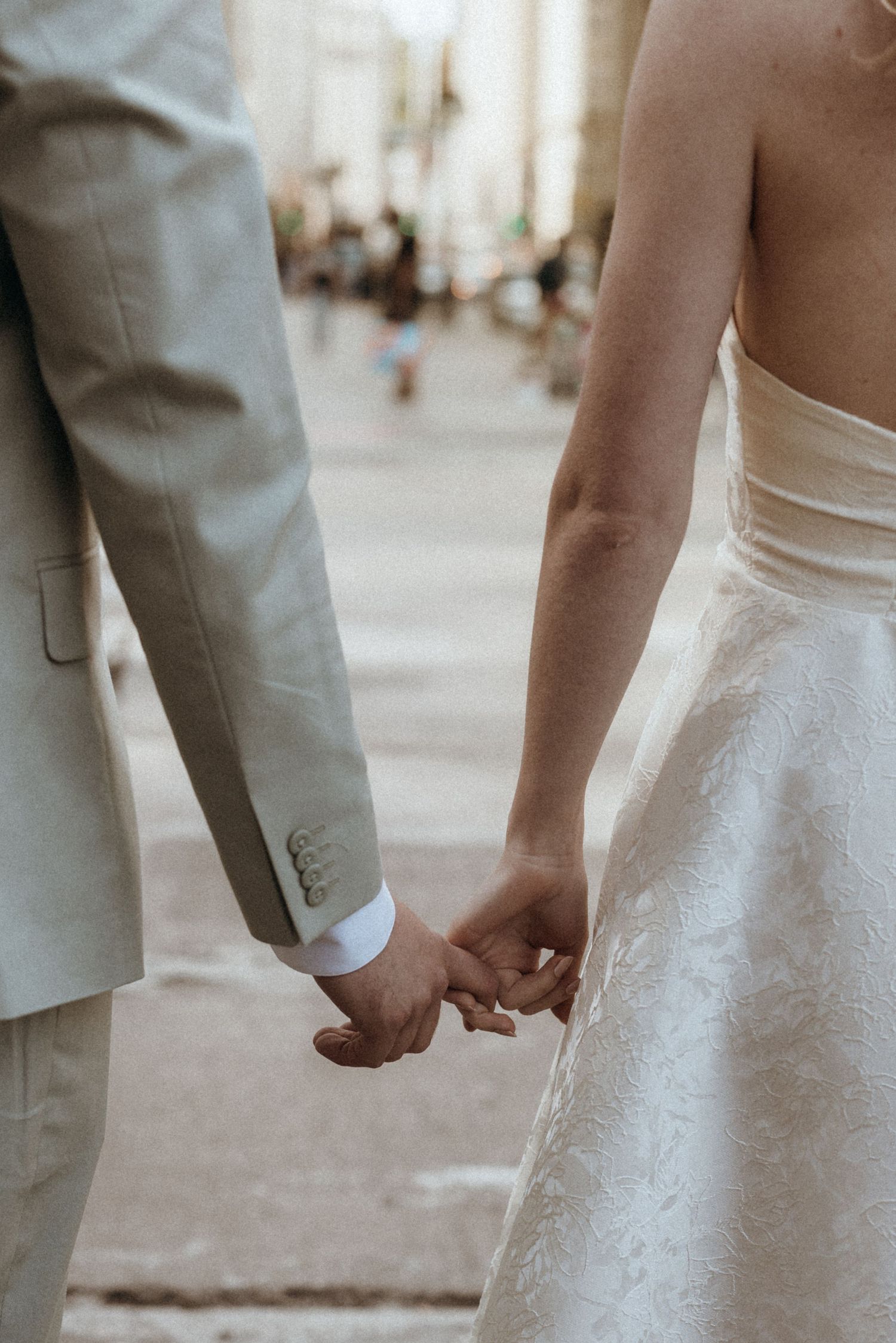 Bride and groom holding hands in wedding attire on a city street, groom in light gray suit.