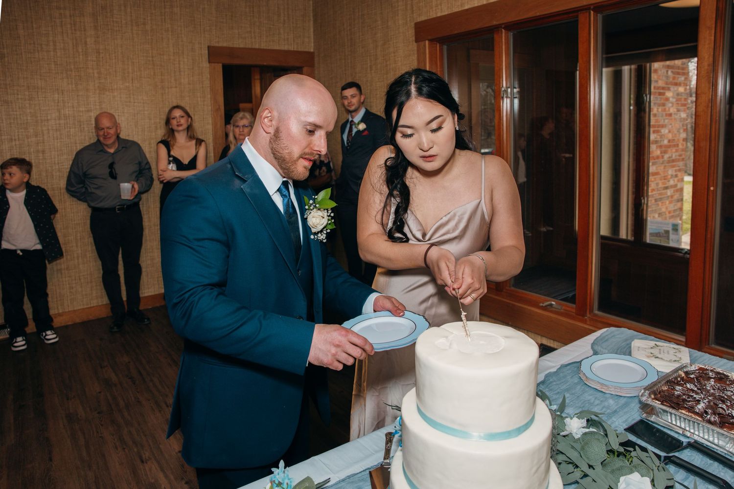 Bride and groom cutting their two-tier white wedding cake with blue ribbon detail at reception.