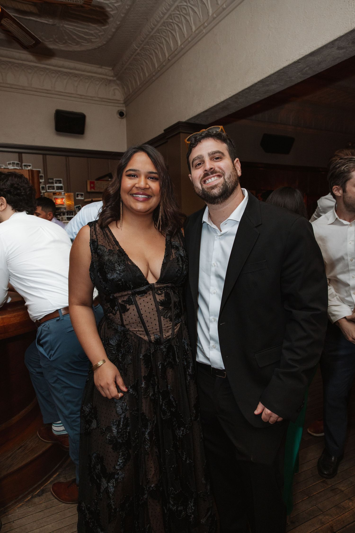 A woman in a black lace dress and a man in a suit smile together at an elegant evening event.