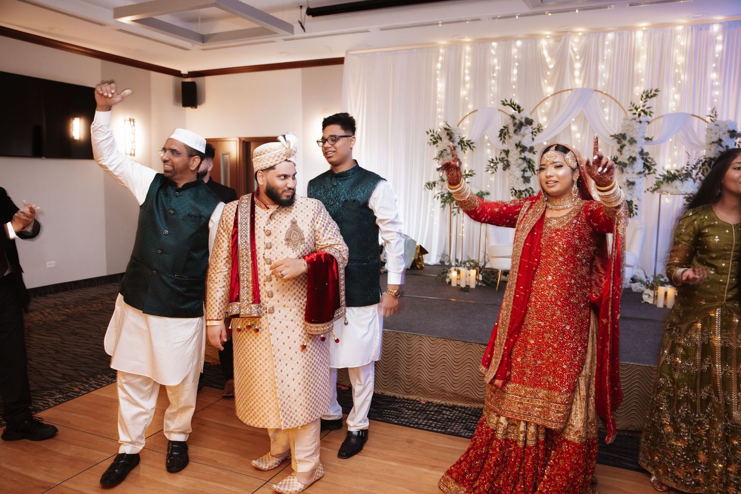 South Asian groom and bride in traditional attire celebrate with guests at wedding reception.