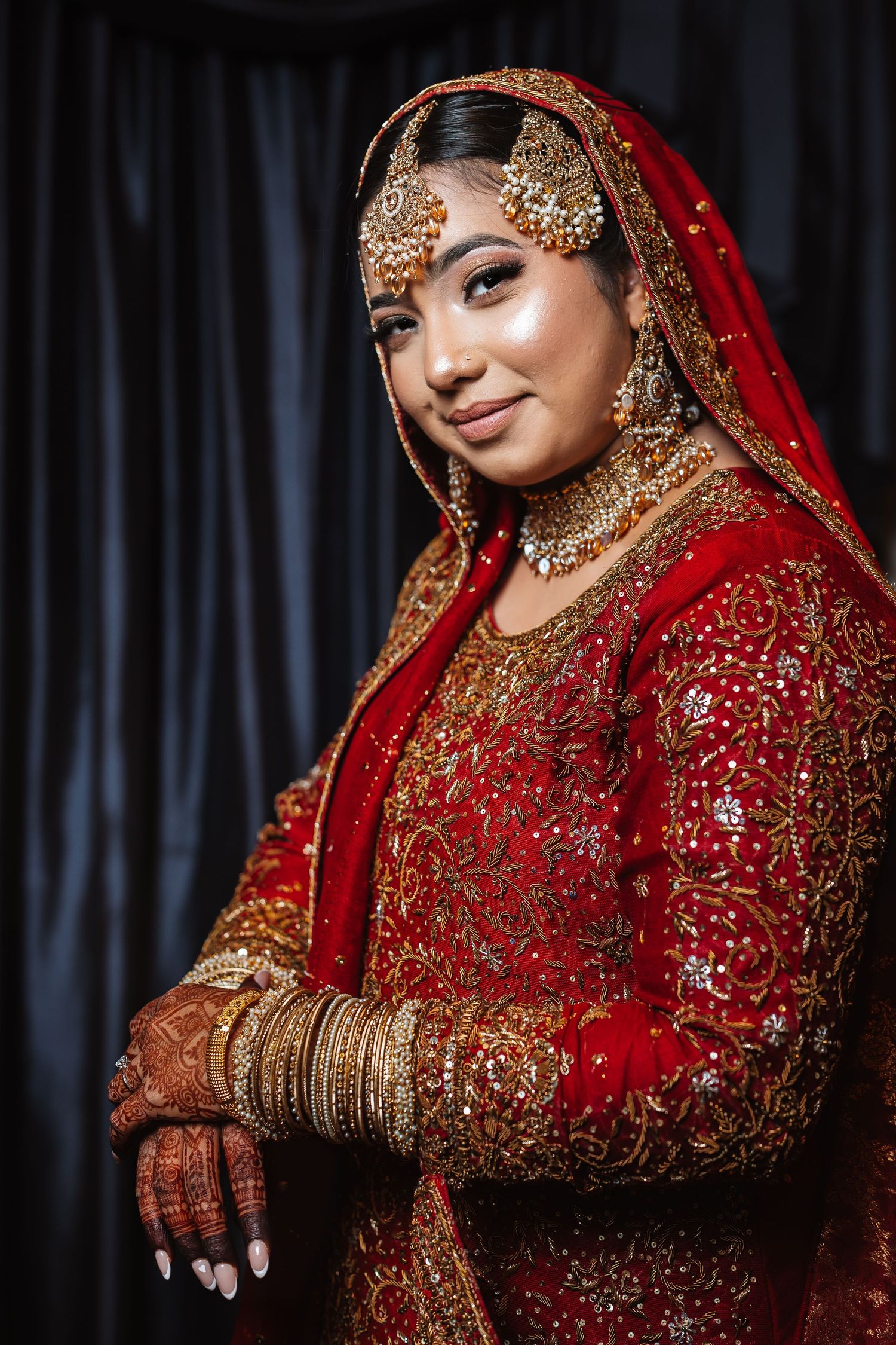 Beautiful Indian bride posing in ornate red and gold bridal lehenga with traditional jewelry and dupatta.