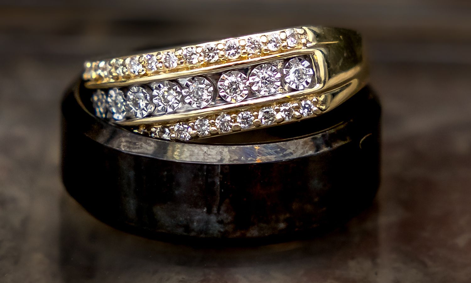 Elegant diamond and gold wedding ring set with black band on reflective surface.