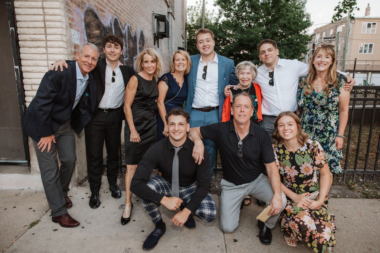 Large family group posing together outdoors near a brick building at a casual gathering.