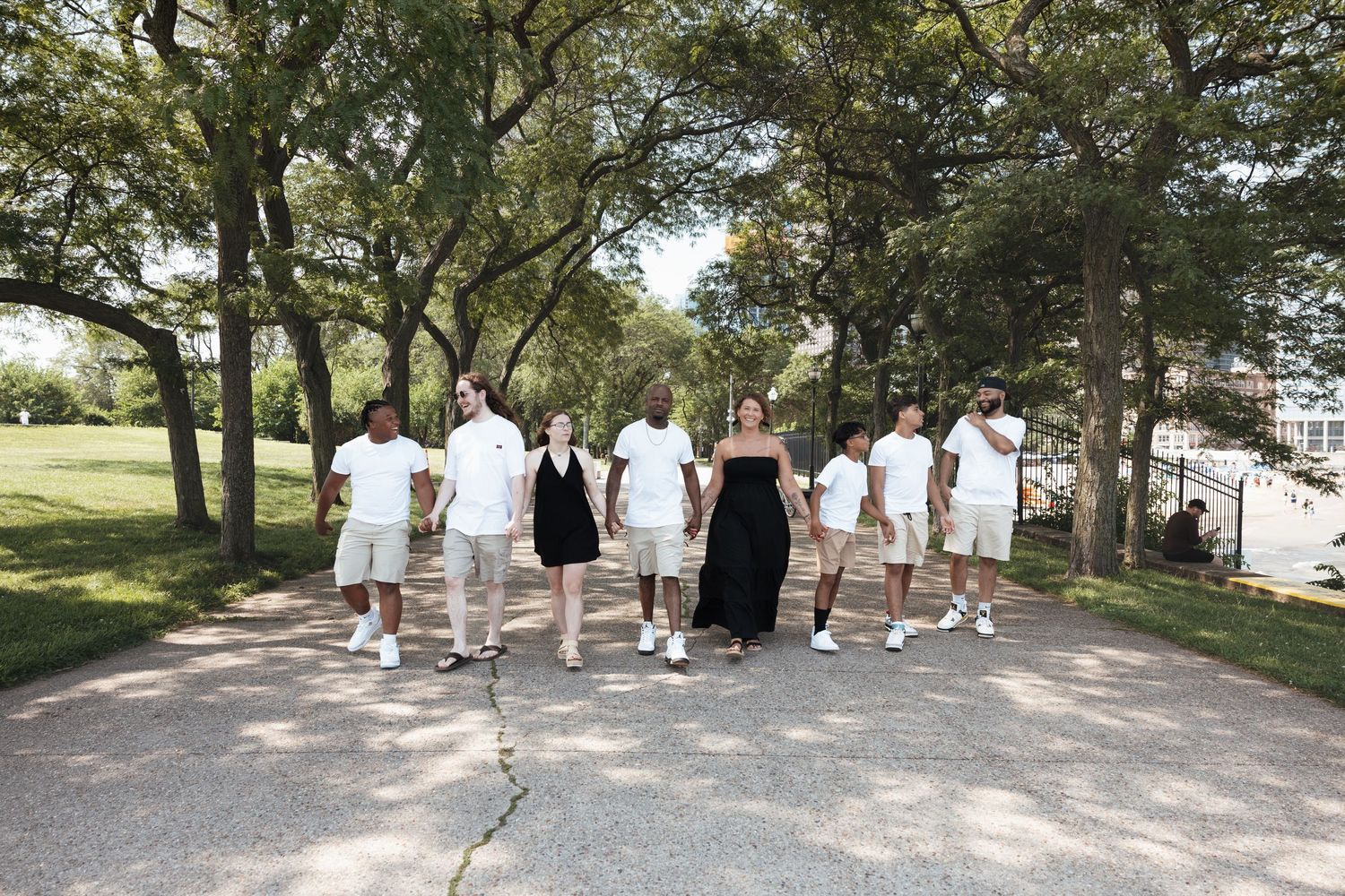 Family group walking together along a tree-lined park path in matching white and beige outfits.