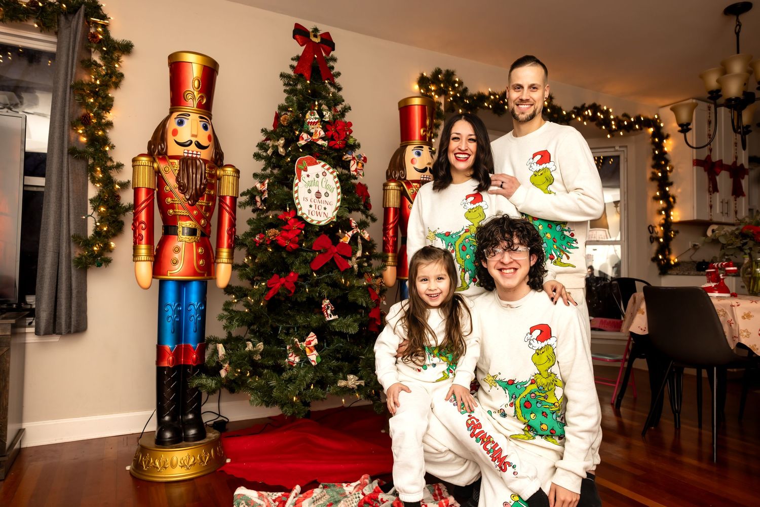 Family smiling in Grinch holiday pajamas beside Christmas tree with nutcracker.