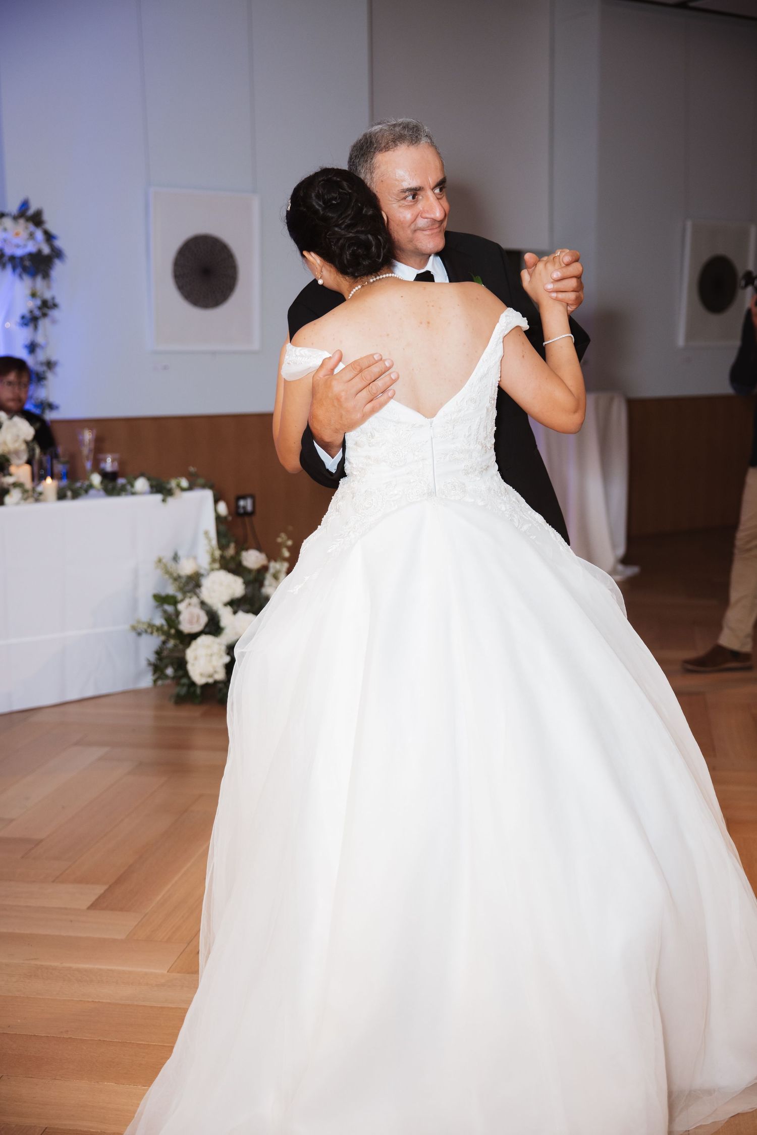 Bride and older man share emotional father-daughter dance at wedding reception on wooden dance floor.
