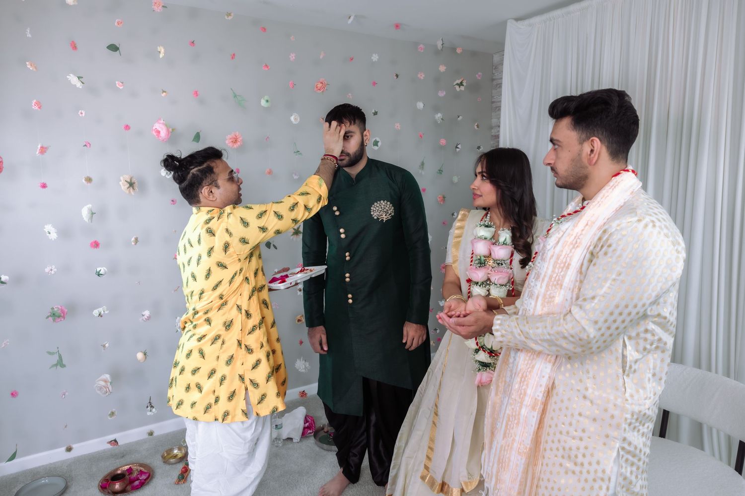 Man in yellow kurta applies tilak on guest's forehead during traditional Indian wedding ceremony.