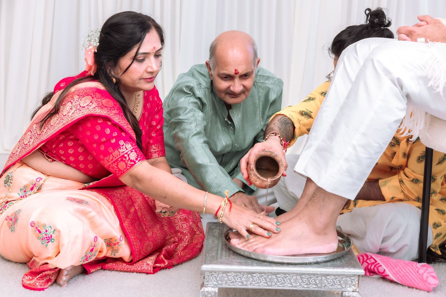 Indian couple performing traditional foot washing ritual during Hindu wedding ceremony with copper vessel.
