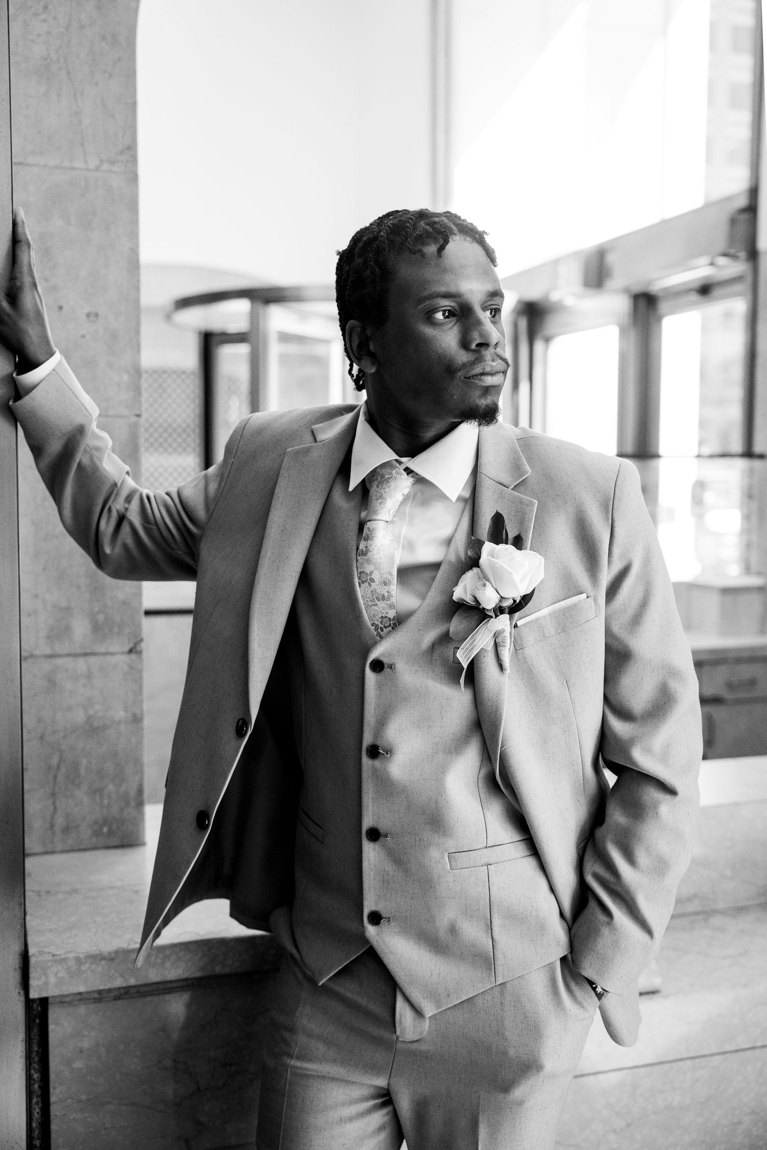 Elegant groom in gray three-piece suit with boutonniere posing in black and white photo.