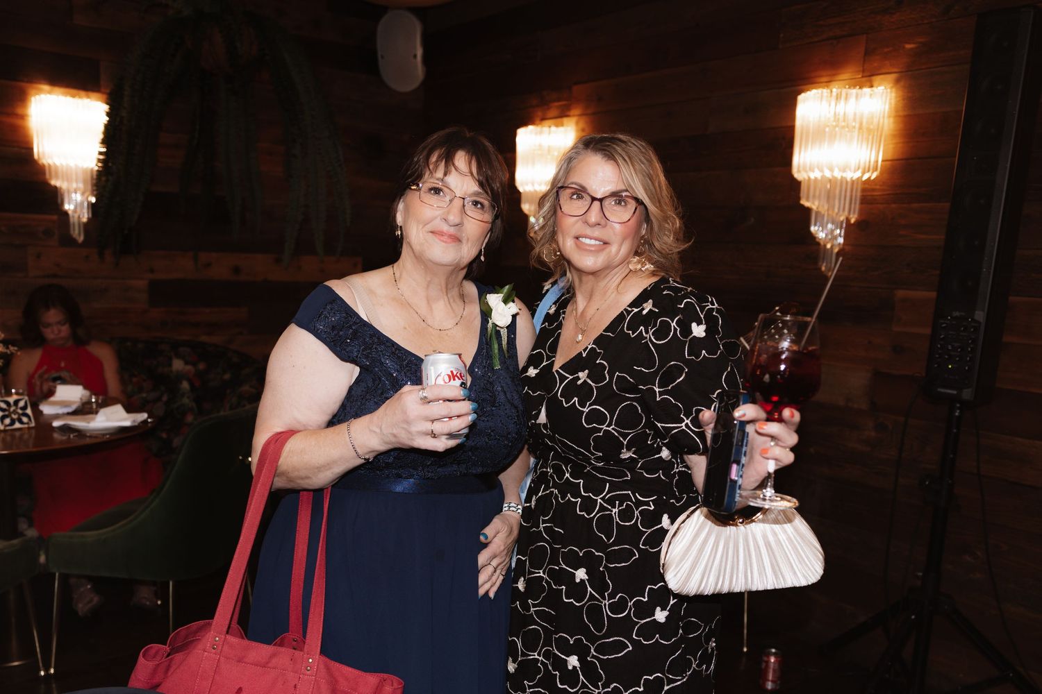 Two women smiling and holding drinks at an elegant wedding reception venue.