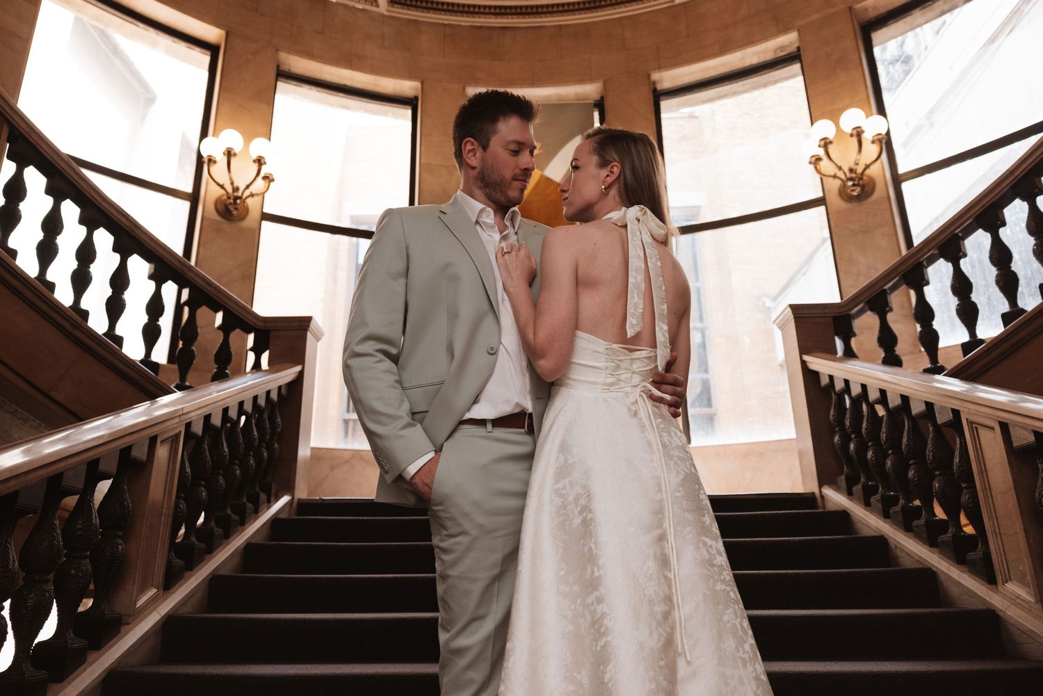 Bride and groom share a romantic moment on grand staircase in stunning wedding attire.