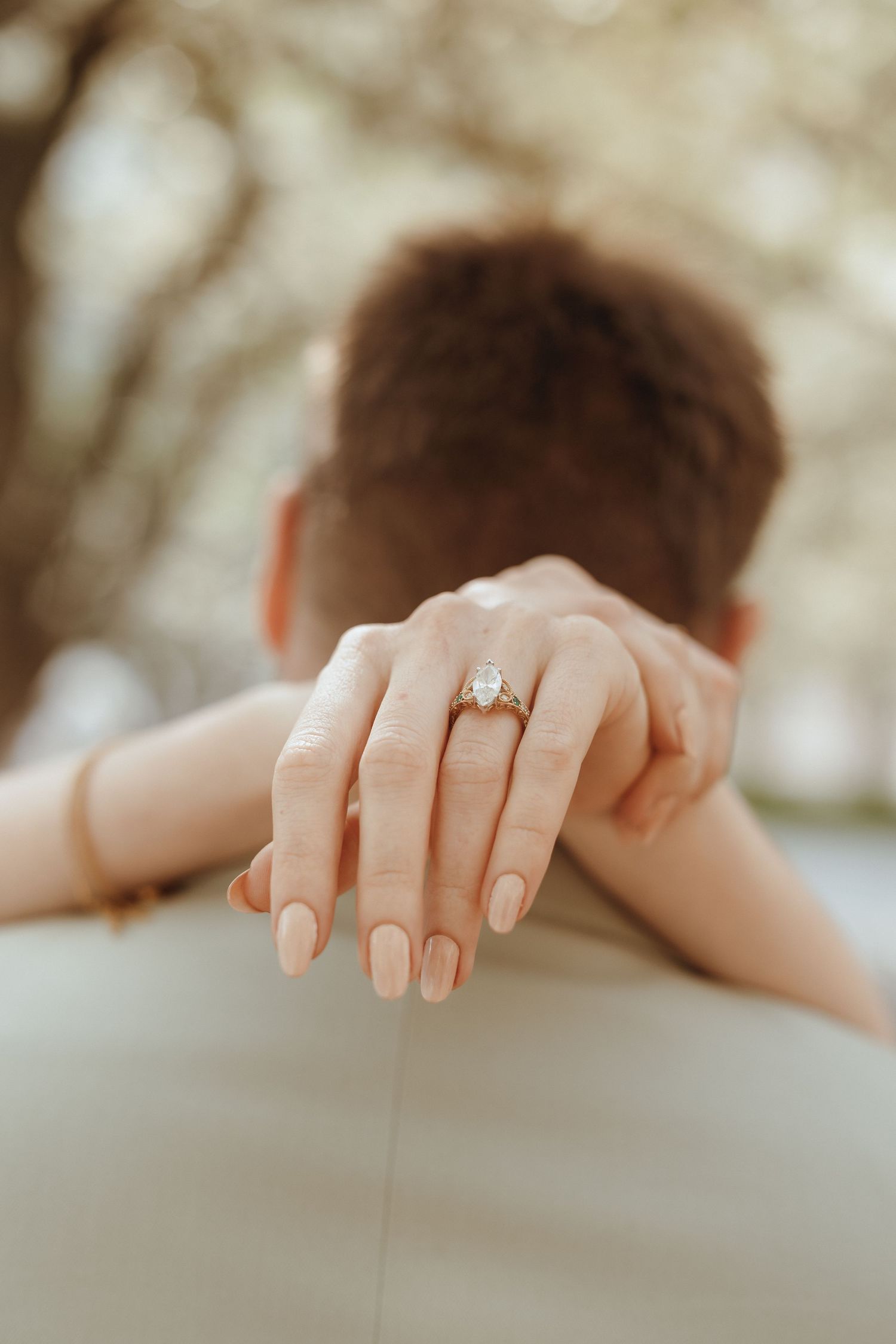 Close-up of bride's hand showing a stunning pear-shaped diamond engagement ring on groom's shoulder.