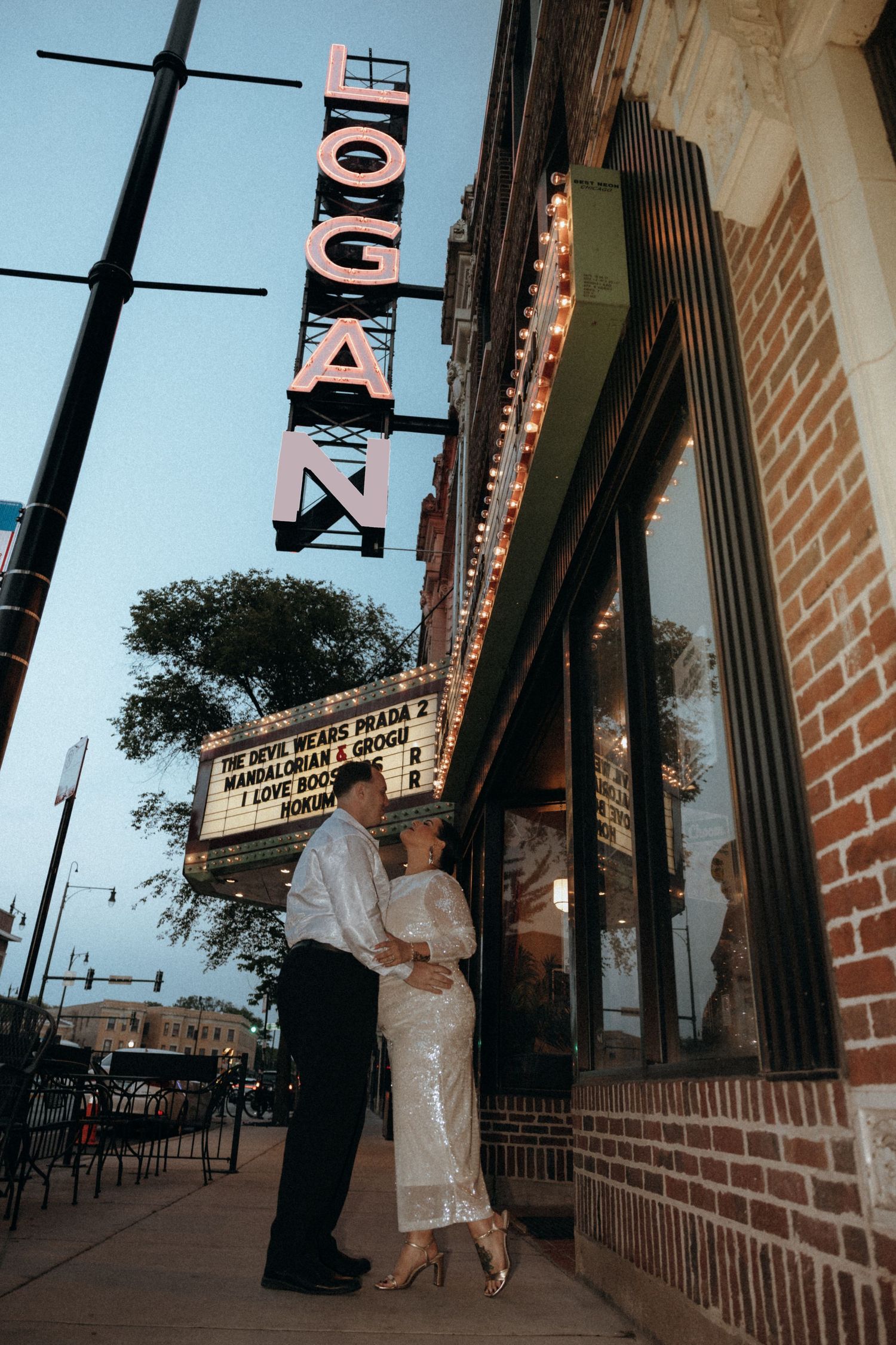 Newlyweds embracing under the glowing Logan Theatre marquee sign at twilight in Chicago.