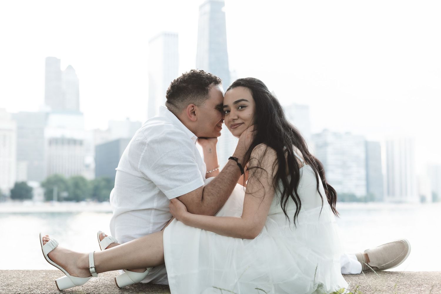 Couple sitting close together by a city waterfront, woman smiling at camera.