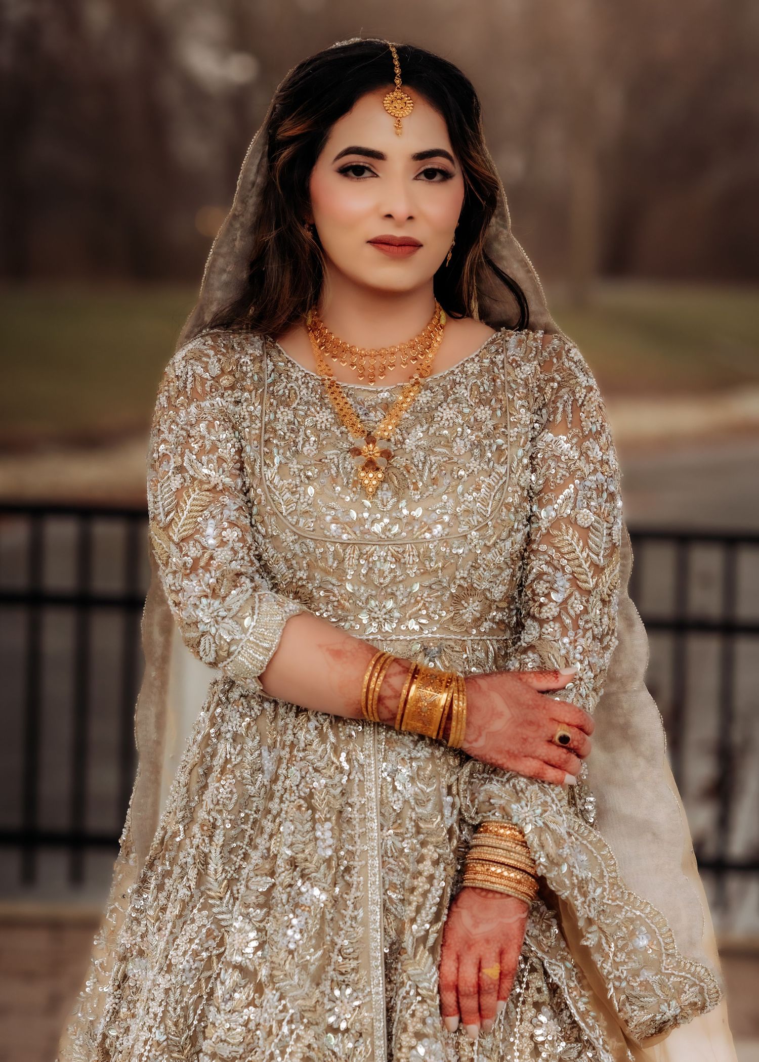 South Asian bride in heavily embroidered gold lehenga with maang tikka and gold jewelry.