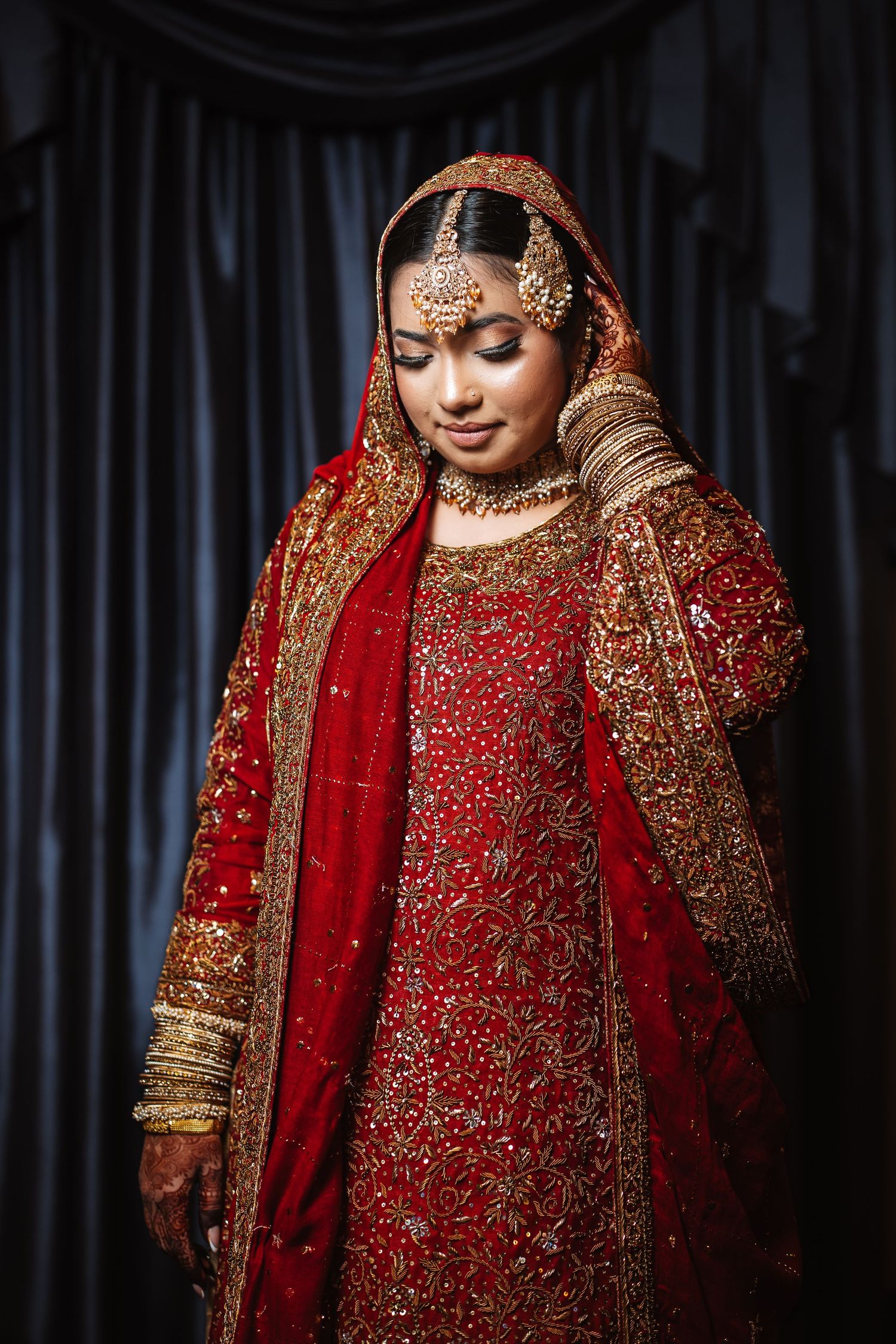 Elegant Indian bride in red and gold embroidered lehenga with traditional bridal jewelry and dupatta.