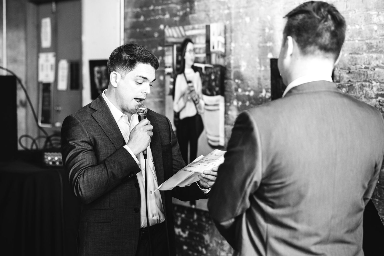 Black and white photo of man speaking into microphone at wedding ceremony.