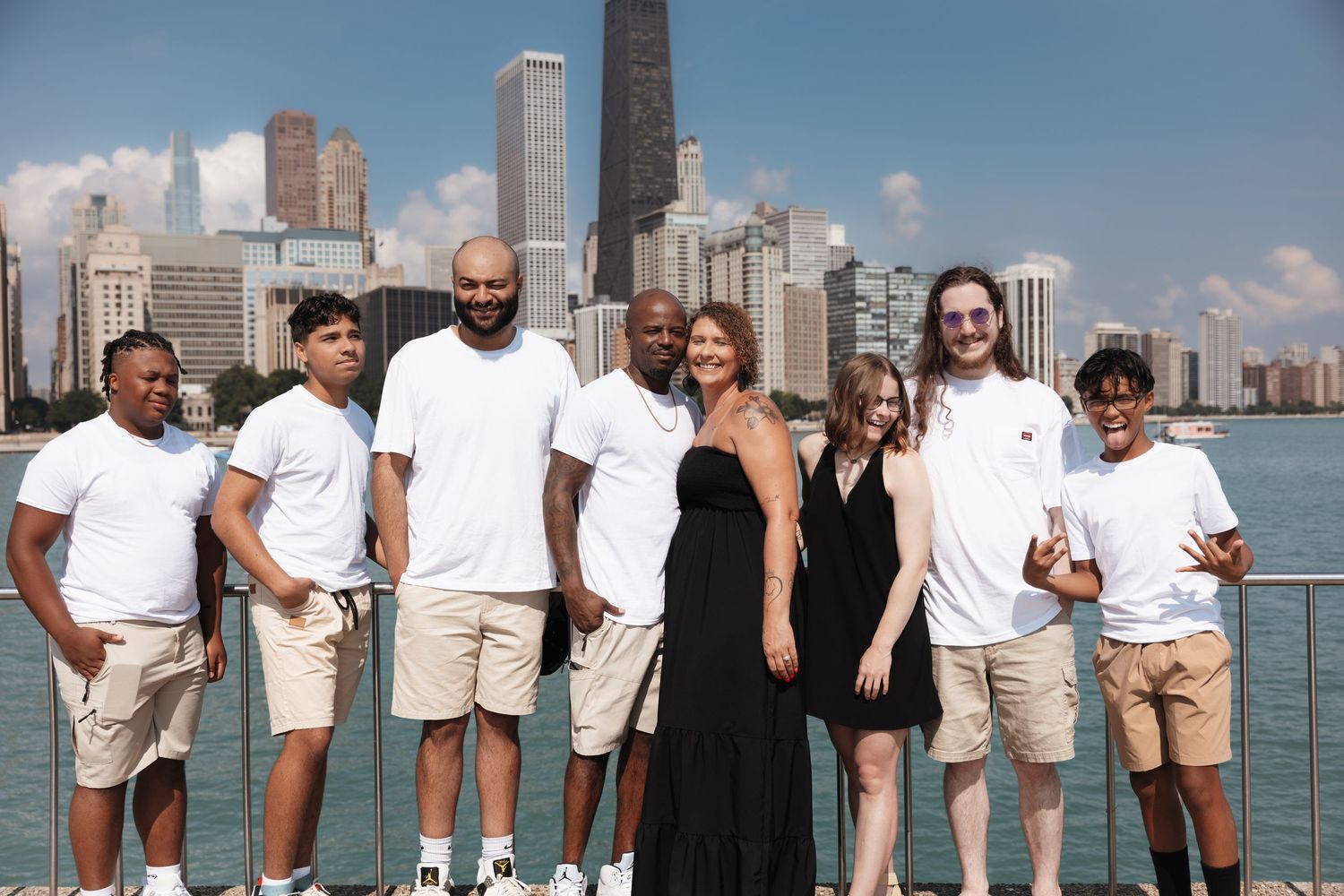 Blended family group of seven posing together by Lake Michigan with Chicago city skyline backdrop.