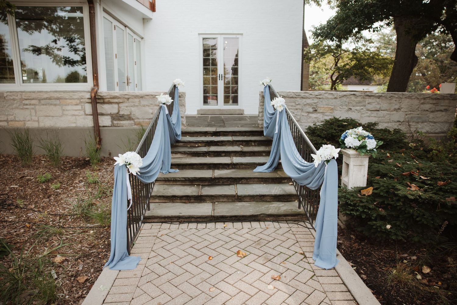 Stone staircase decorated with dusty blue fabric draping and white floral arrangements for a wedding.