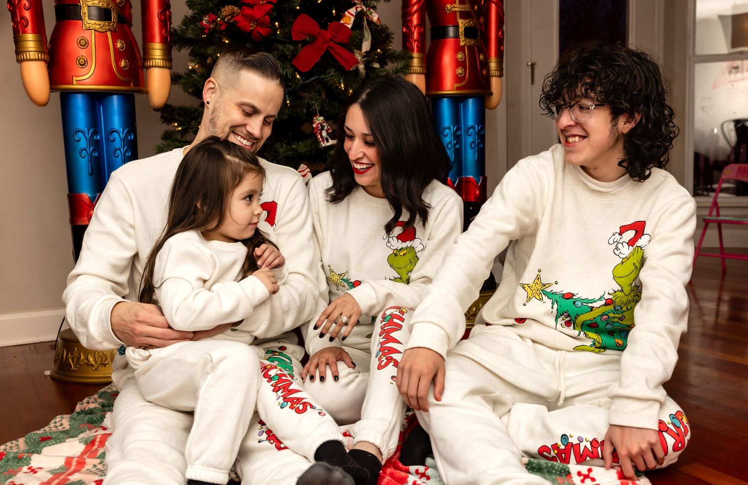Happy family of four in coordinating white Grinch Christmas pajamas smiling by holiday tree.