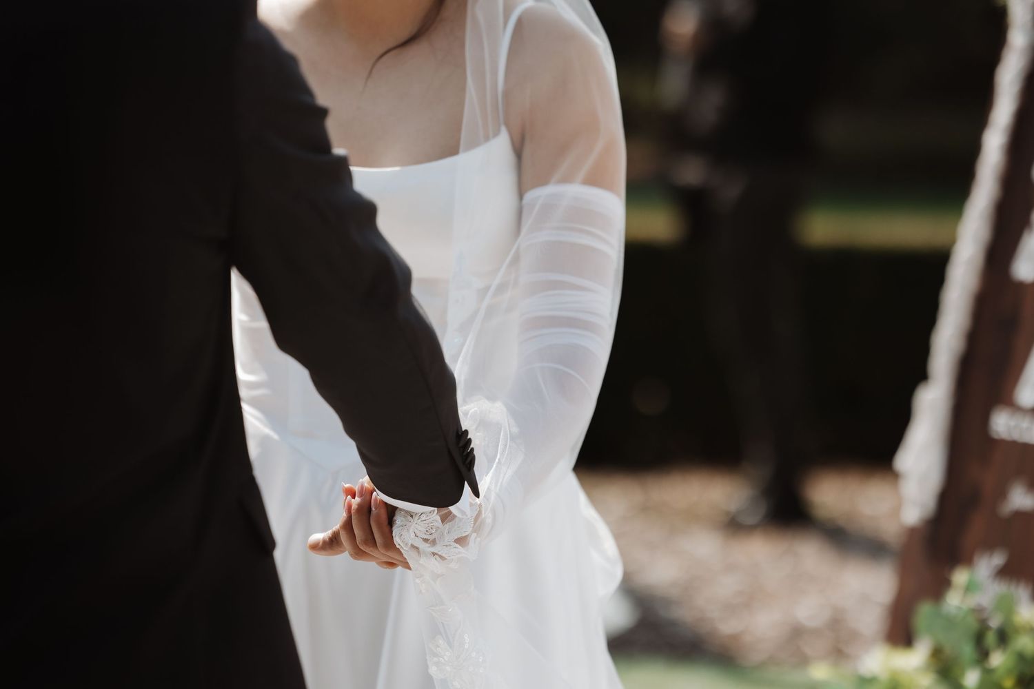 Bride and groom holding hands during outdoor wedding ceremony, bride wearing white gloves.