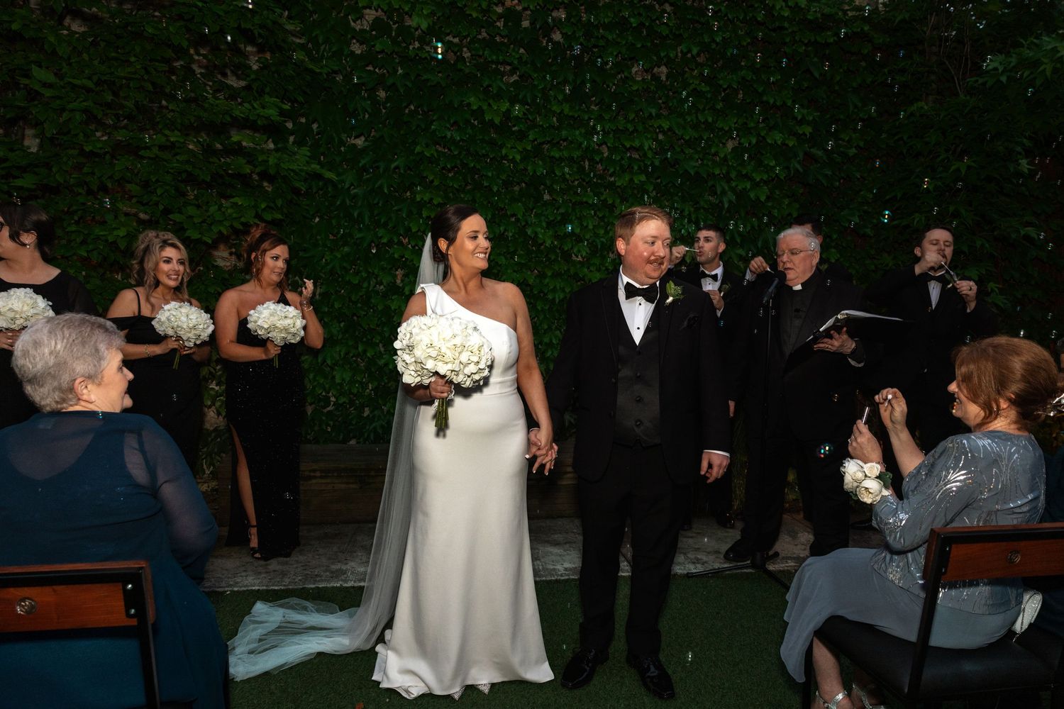 Newlywed couple walks back down aisle as guests applaud at outdoor wedding ceremony.