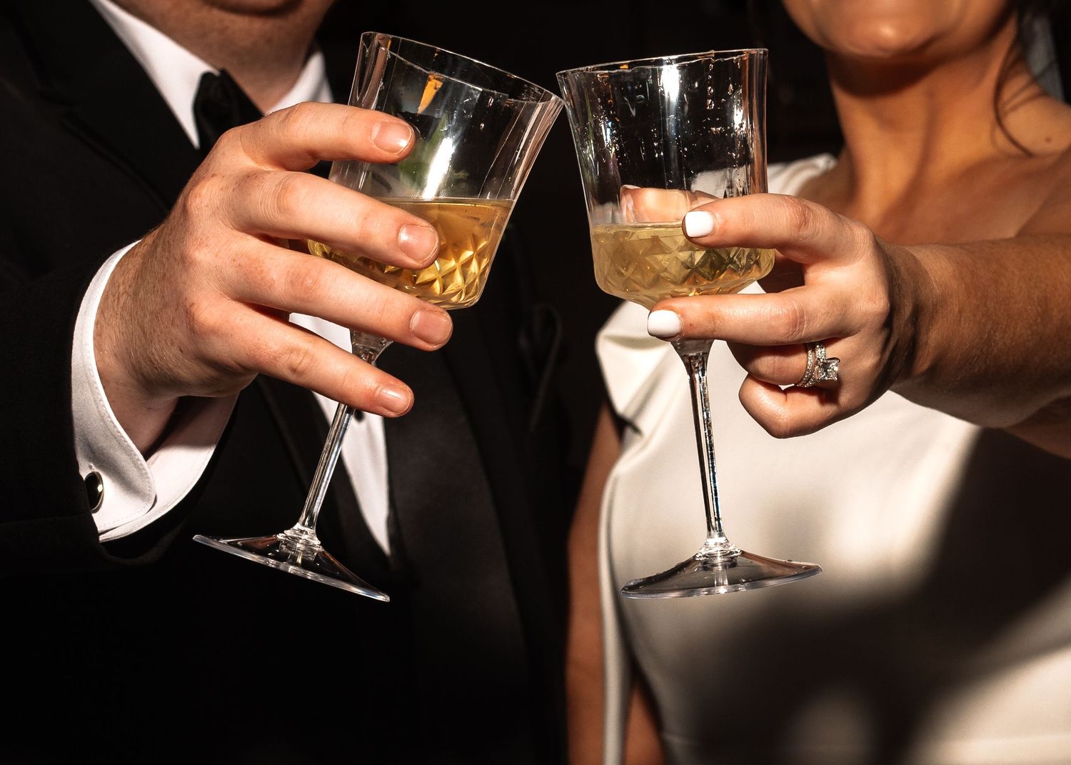 Close-up of bride and groom clinking champagne glasses together in a celebratory wedding toast.