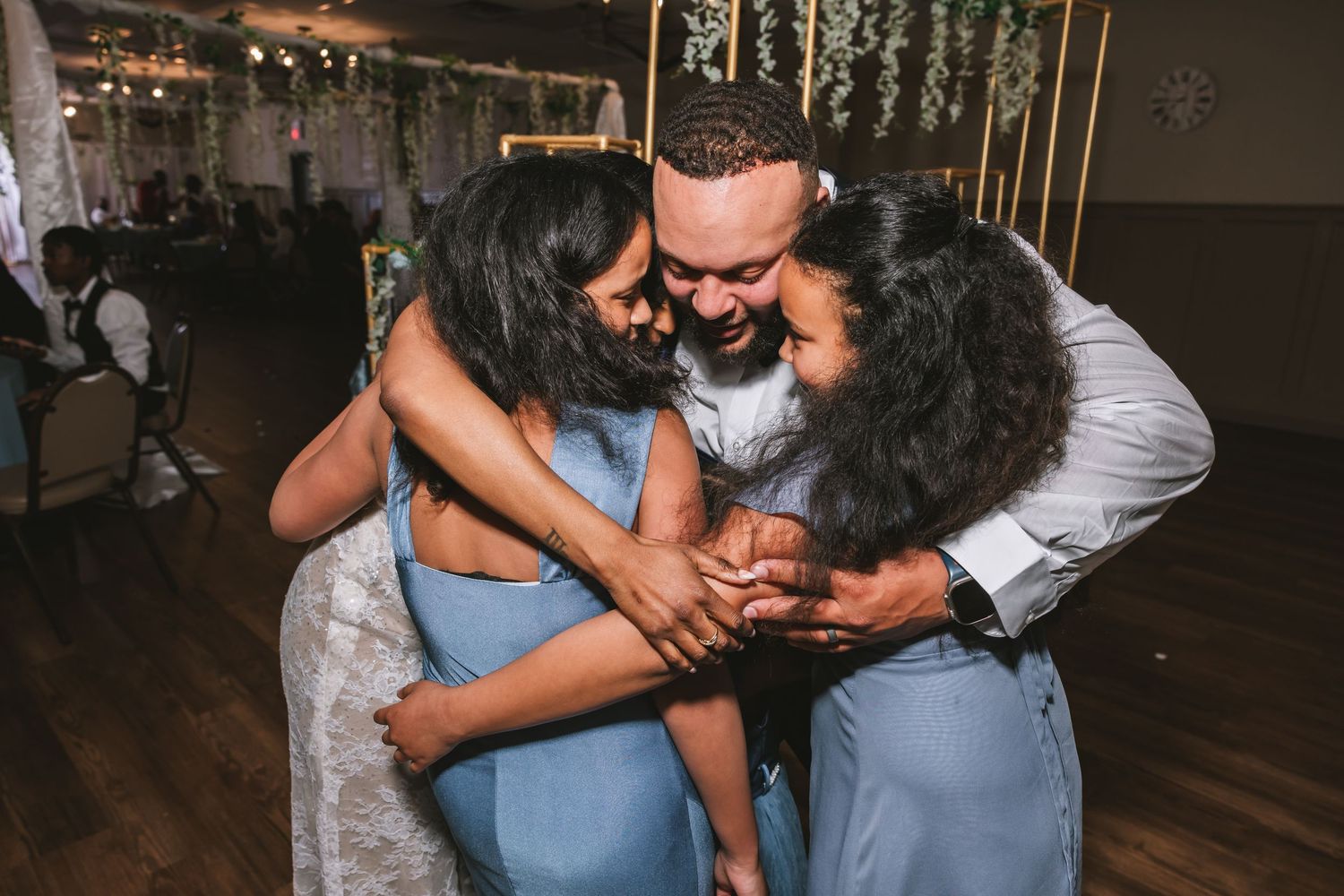 Three people sharing a warm group hug at a wedding celebration.