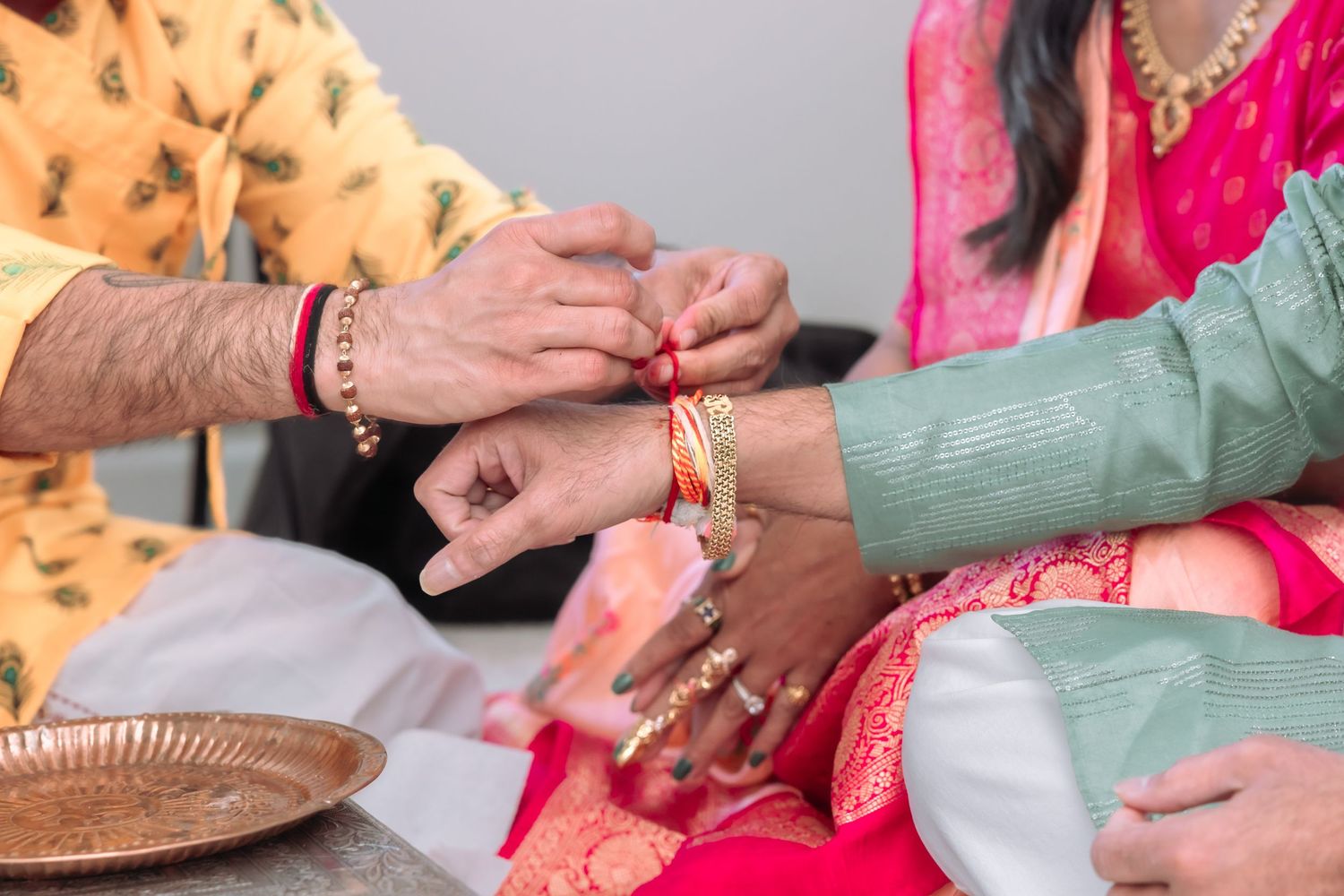 Close-up of hands tying red rakhi bracelet during Indian Hindu ceremony in traditional attire.