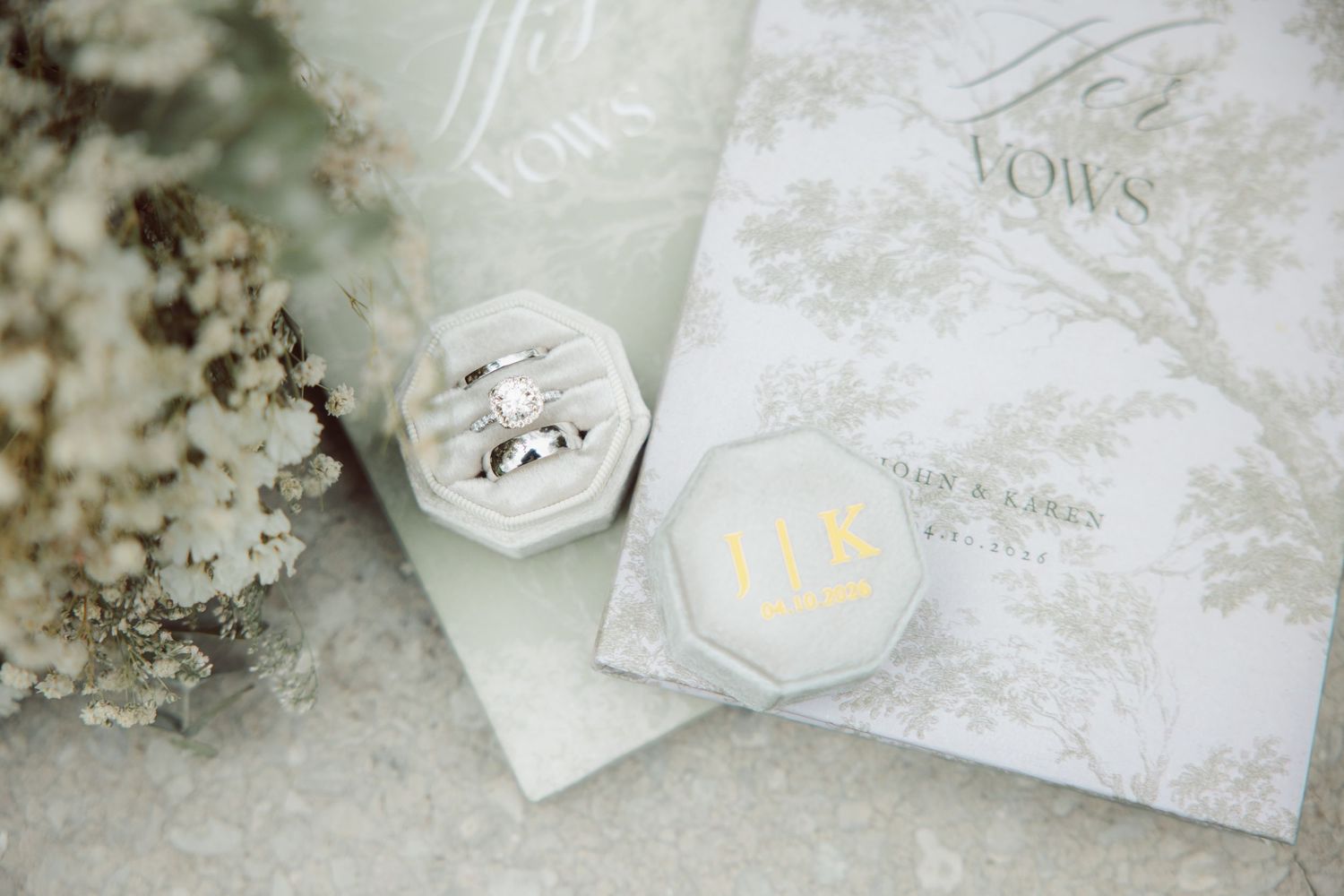 Elegant wedding flat lay with diamond engagement ring in velvet box, vow books, and delicate white flowers.