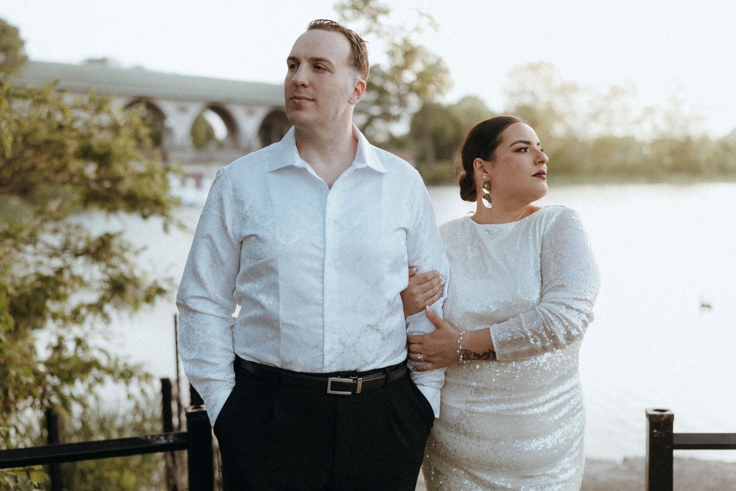 Bride and groom share a romantic moment by a scenic waterfront at golden hour.