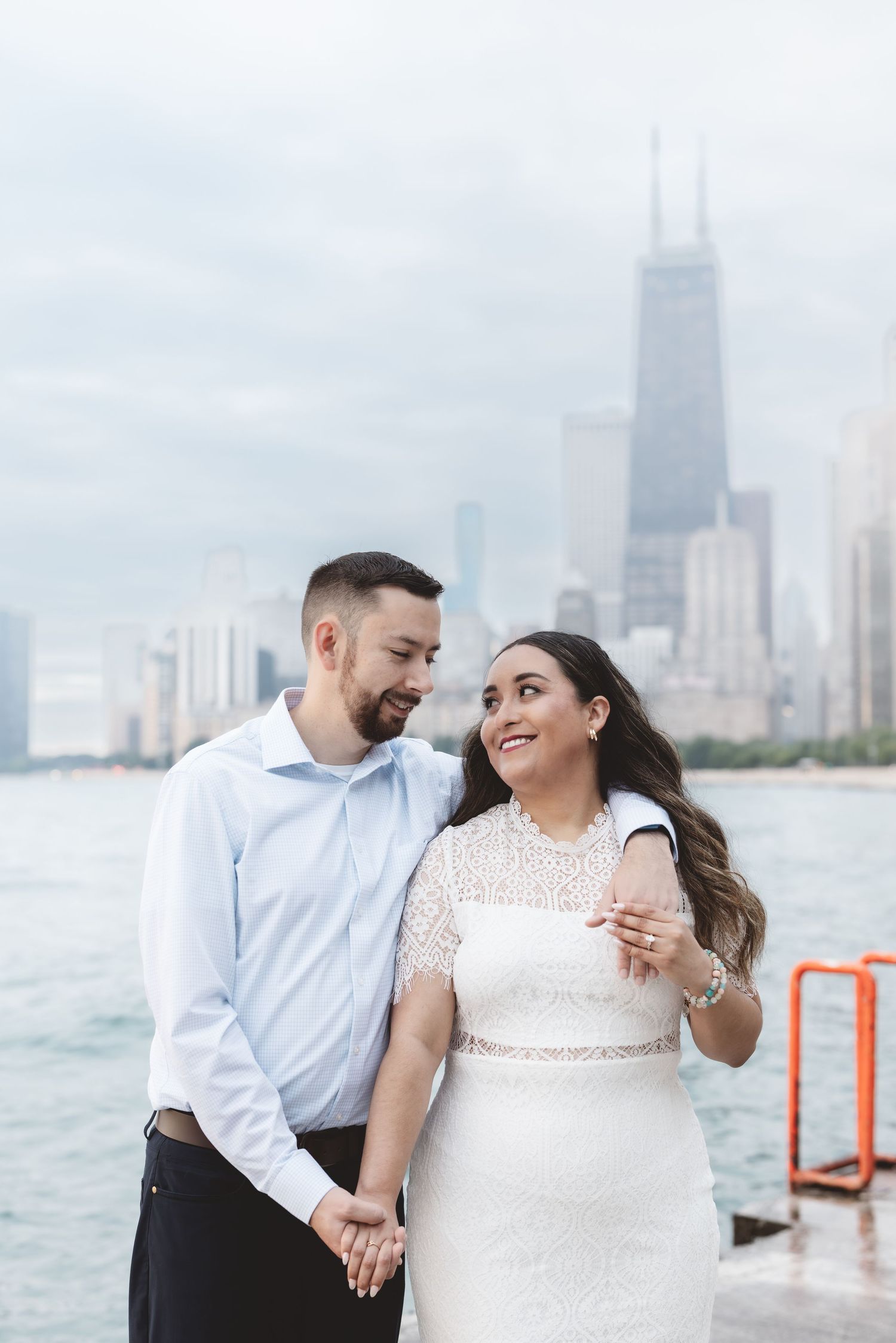 Couple holding hands and embracing with Chicago skyline and John Hancock Center in background on cloudy day.