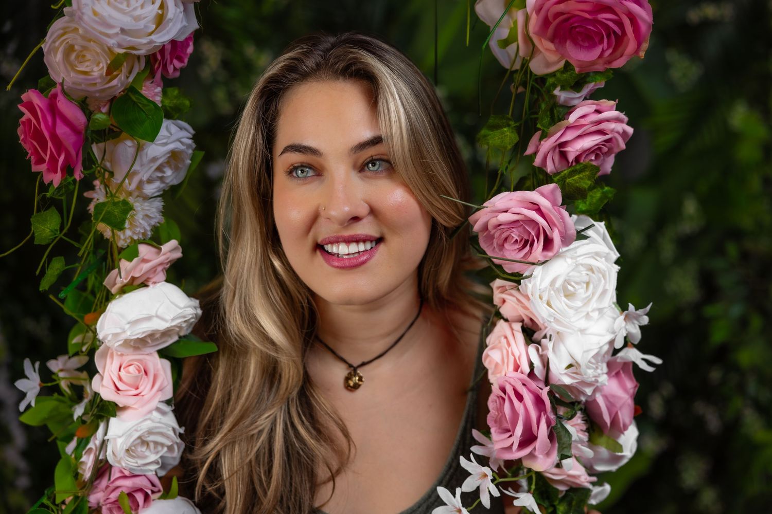 Smiling blonde woman with blue eyes posing among pink and white roses on floral arch backdrop.
